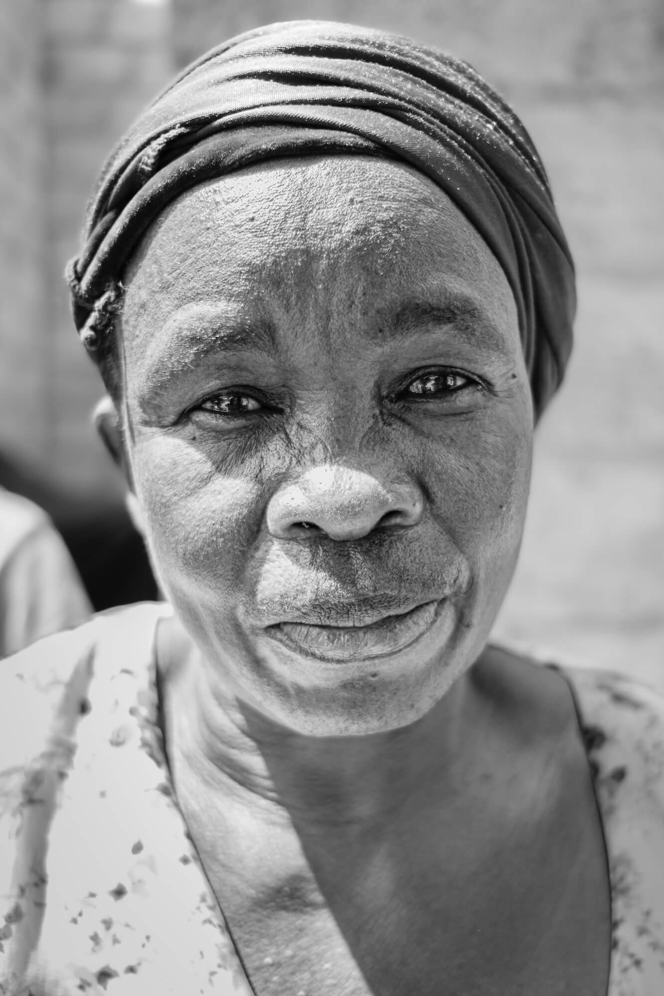 Close-up black and white photo of a Zambian woman wearing a headscarf, smiling gently.