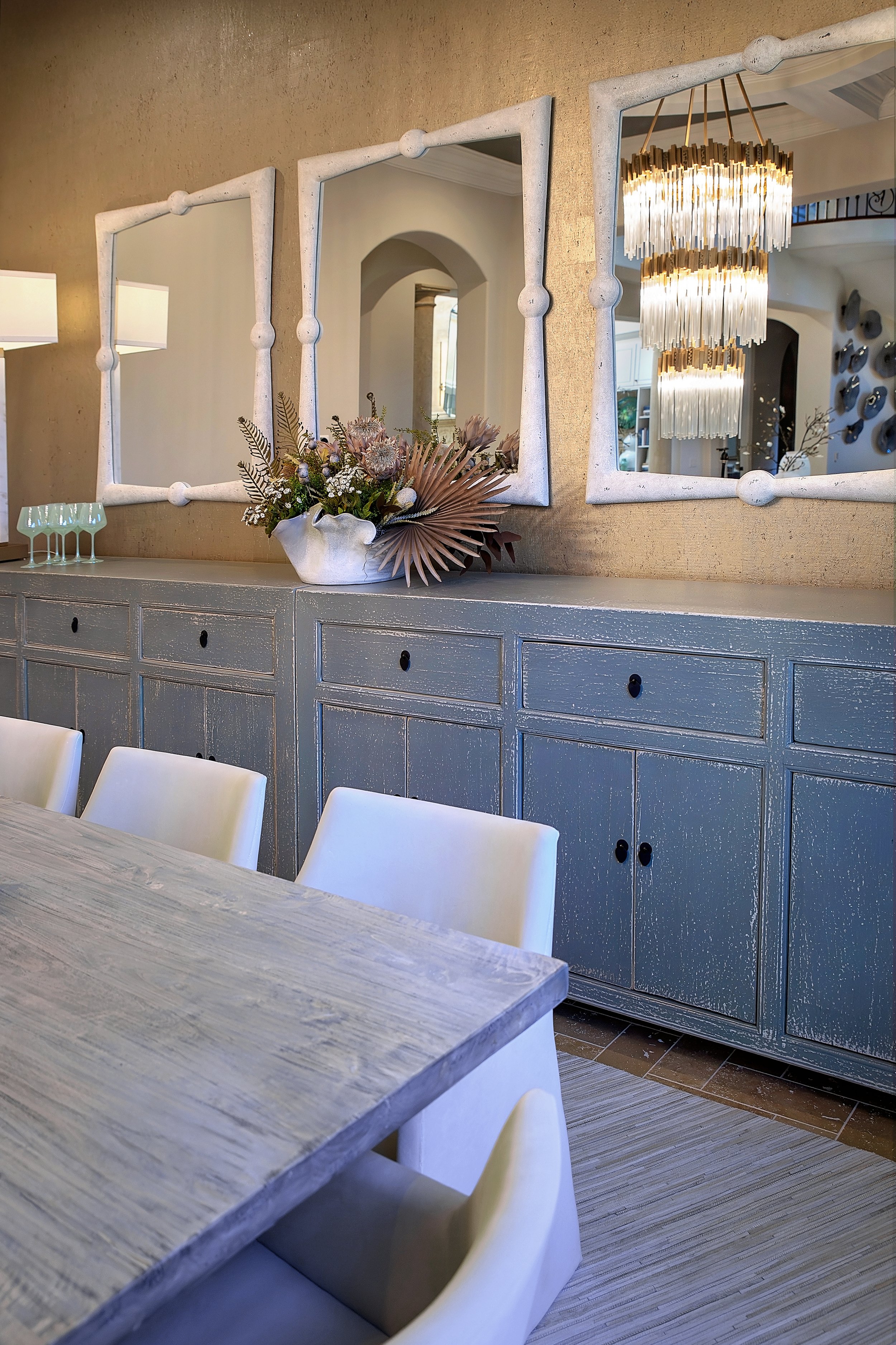 Custom dining room sideboard styled with decorative florals and three statement mirrors reflecting a crystal chandelier