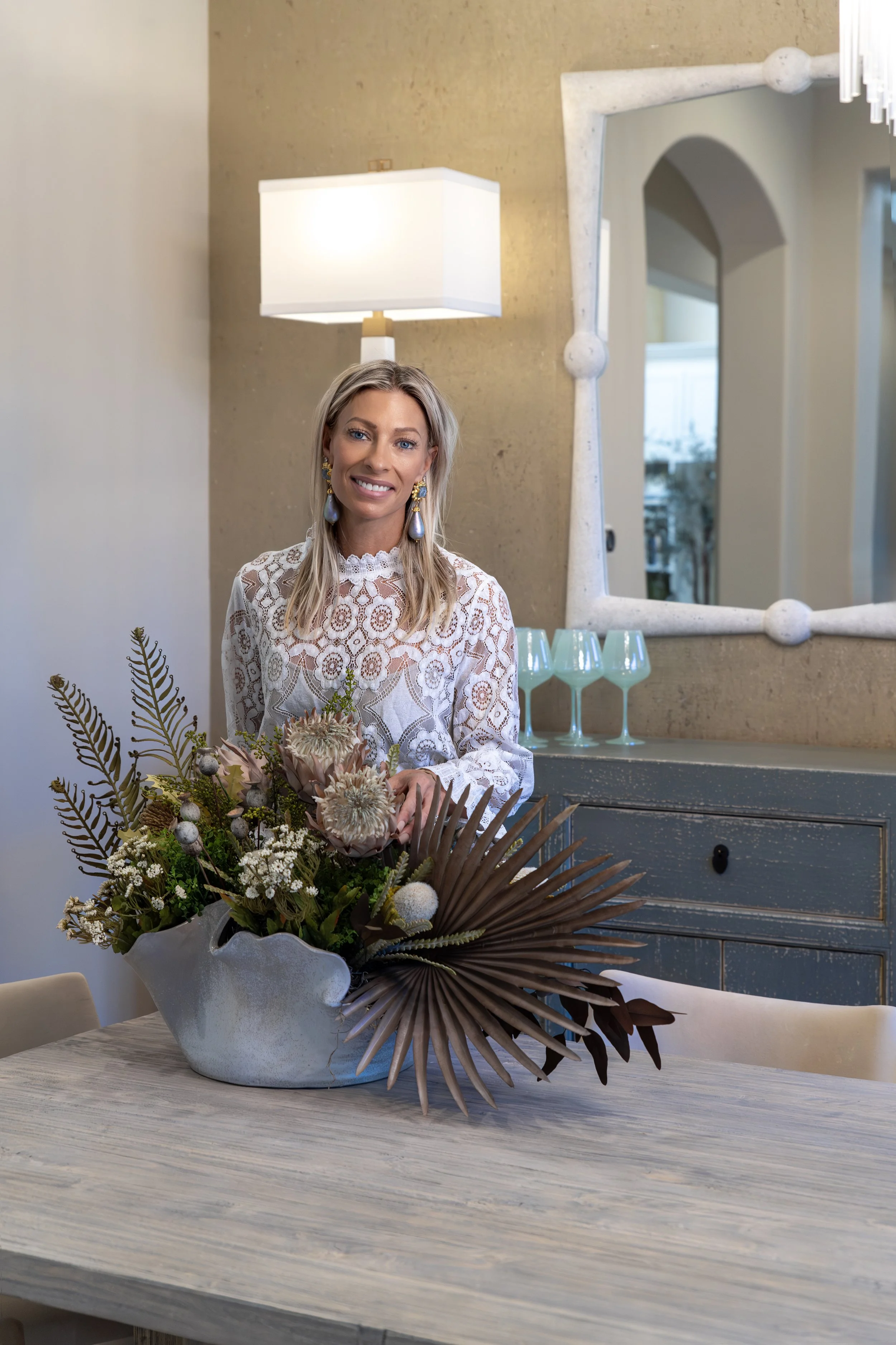 Interior designer standing beside a custom floral arrangement in a luxury dining room with layered textures and curated furnishings