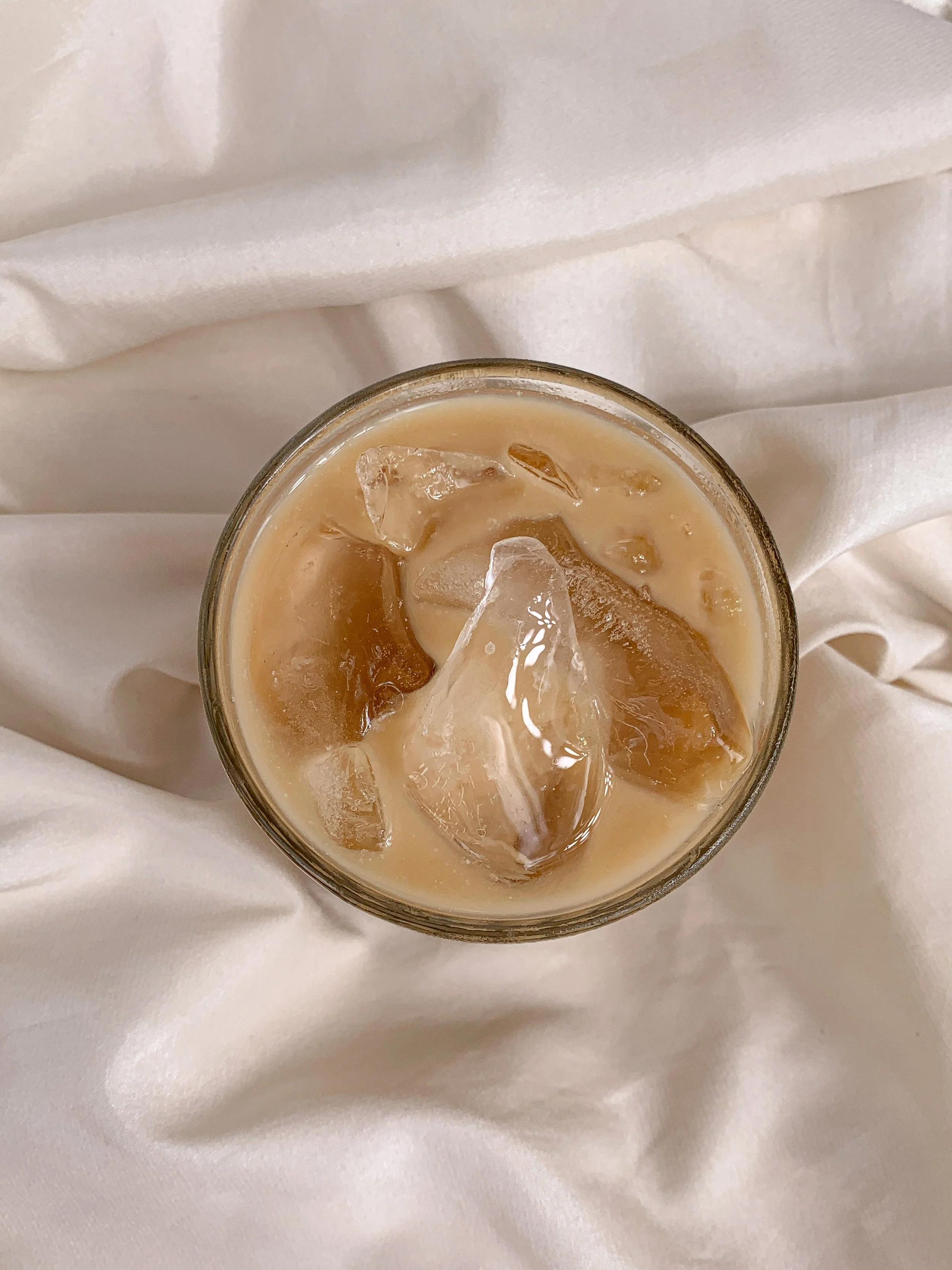 Glass of iced coffee with milk on crumpled white fabric