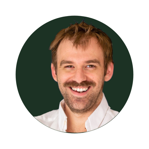 Jamie Brindle, Smiling man with a beard, wearing a white shirt, on a dark background.