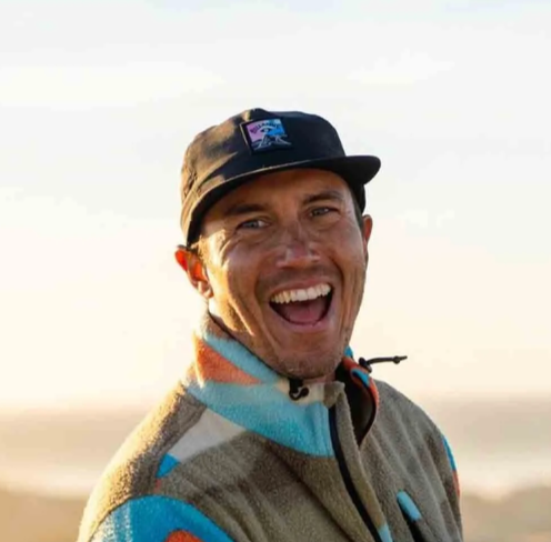 Man smiling outdoors wearing a black cap and a colorful fleece jacket.