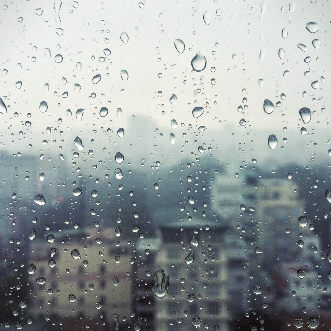 Rain droplets on a window with a blurred cityscape in the background.