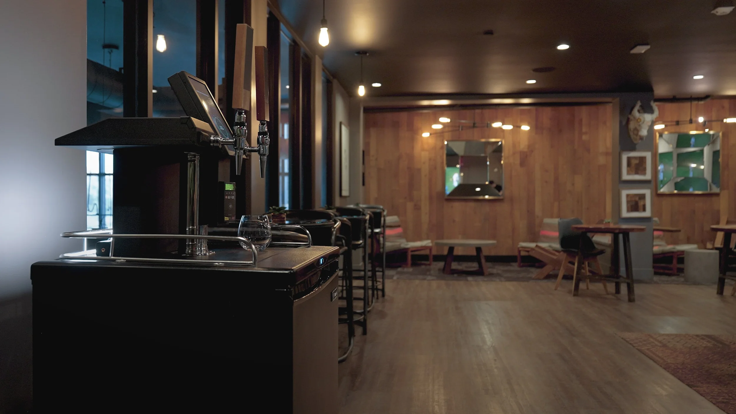 An empty restaurant or bar with a wooden interior, tables, chairs, wall art, and a beverage station with beer taps.