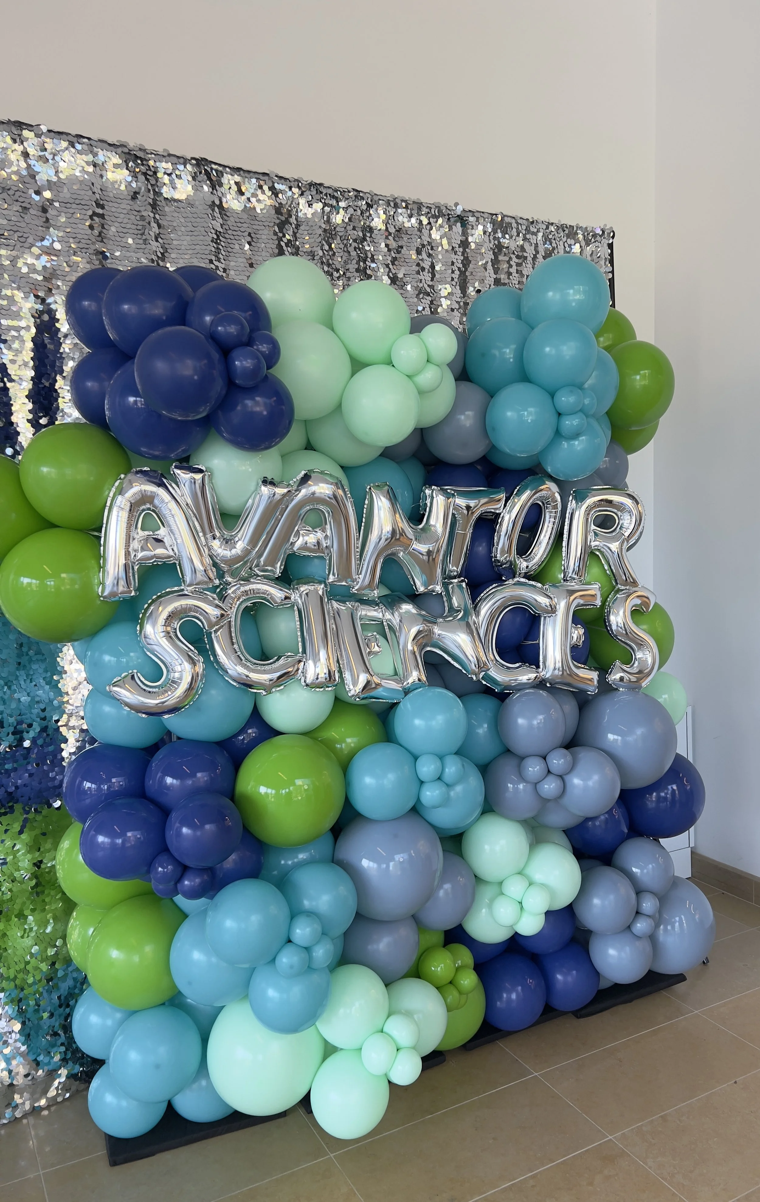 Balloon wall with green, blue, and gray balloons, silver foil balloons spelling 'AVANTOR SCIENCES', and a sequin backdrop.