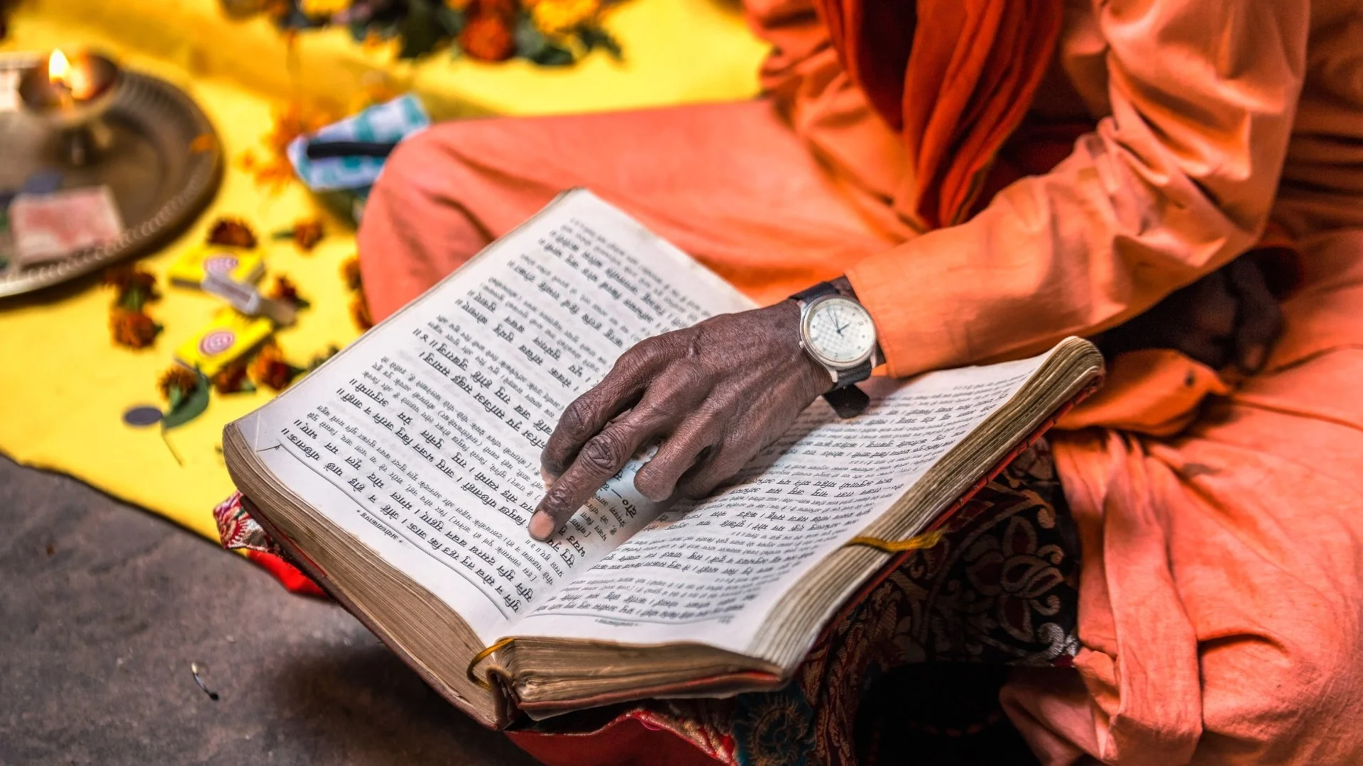 Mão de homem passando pelas letras em sânscrito em um livro em viagem à India com Arca Jornadas