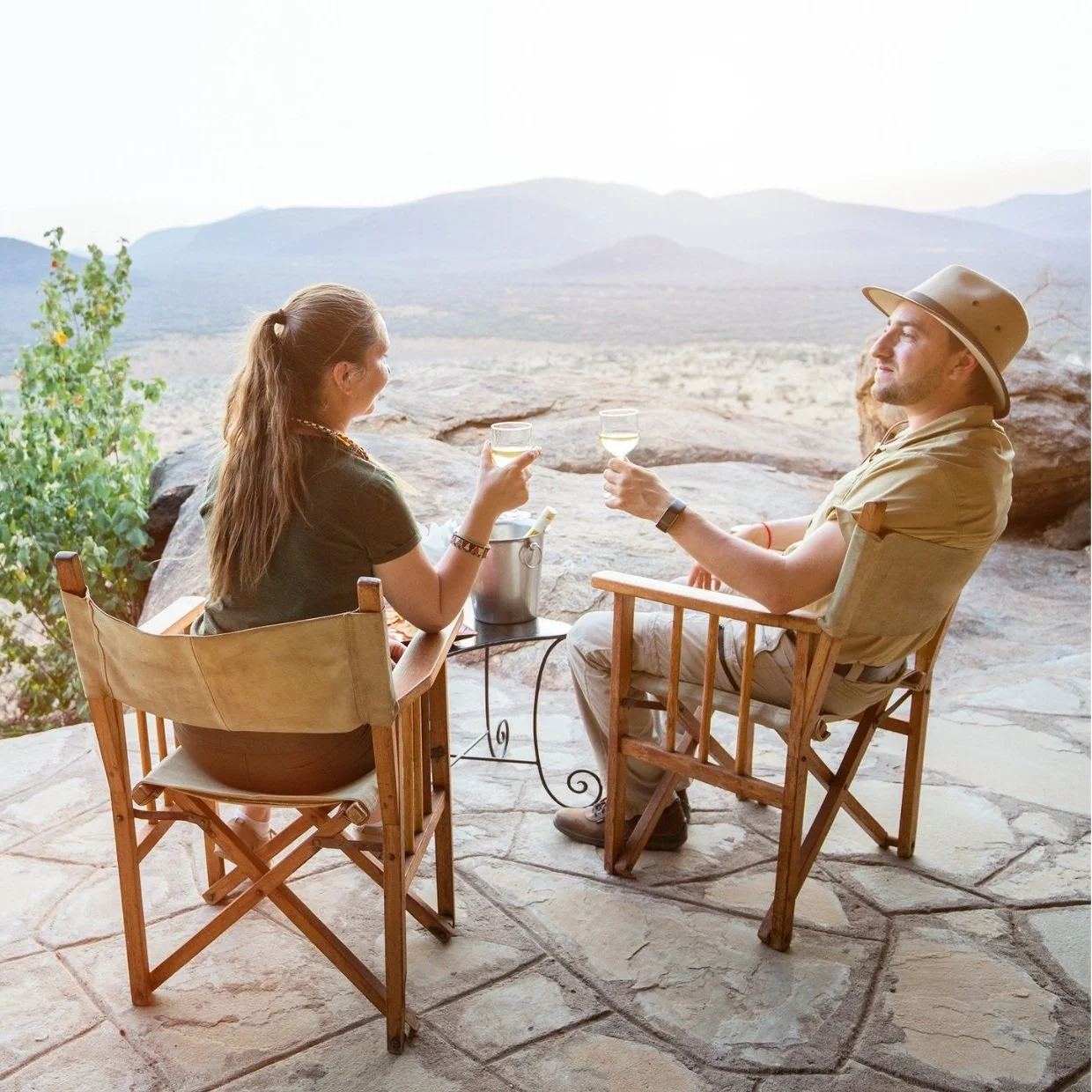 Casal faz um brinde ao por-do-sol com montanhas ao fundo