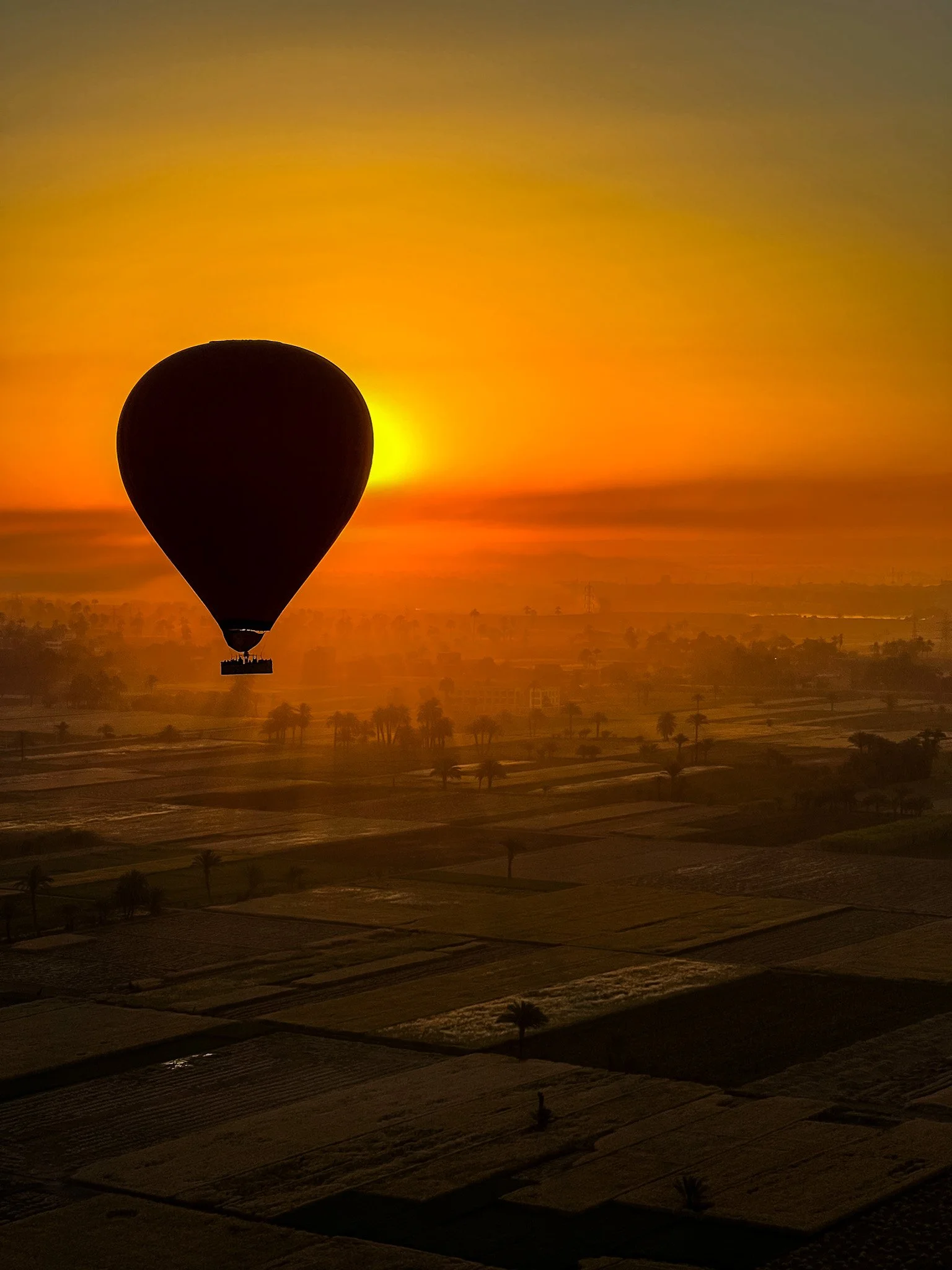 Balão de ar quente sobrevoa os campos de Luxor no amanhecer