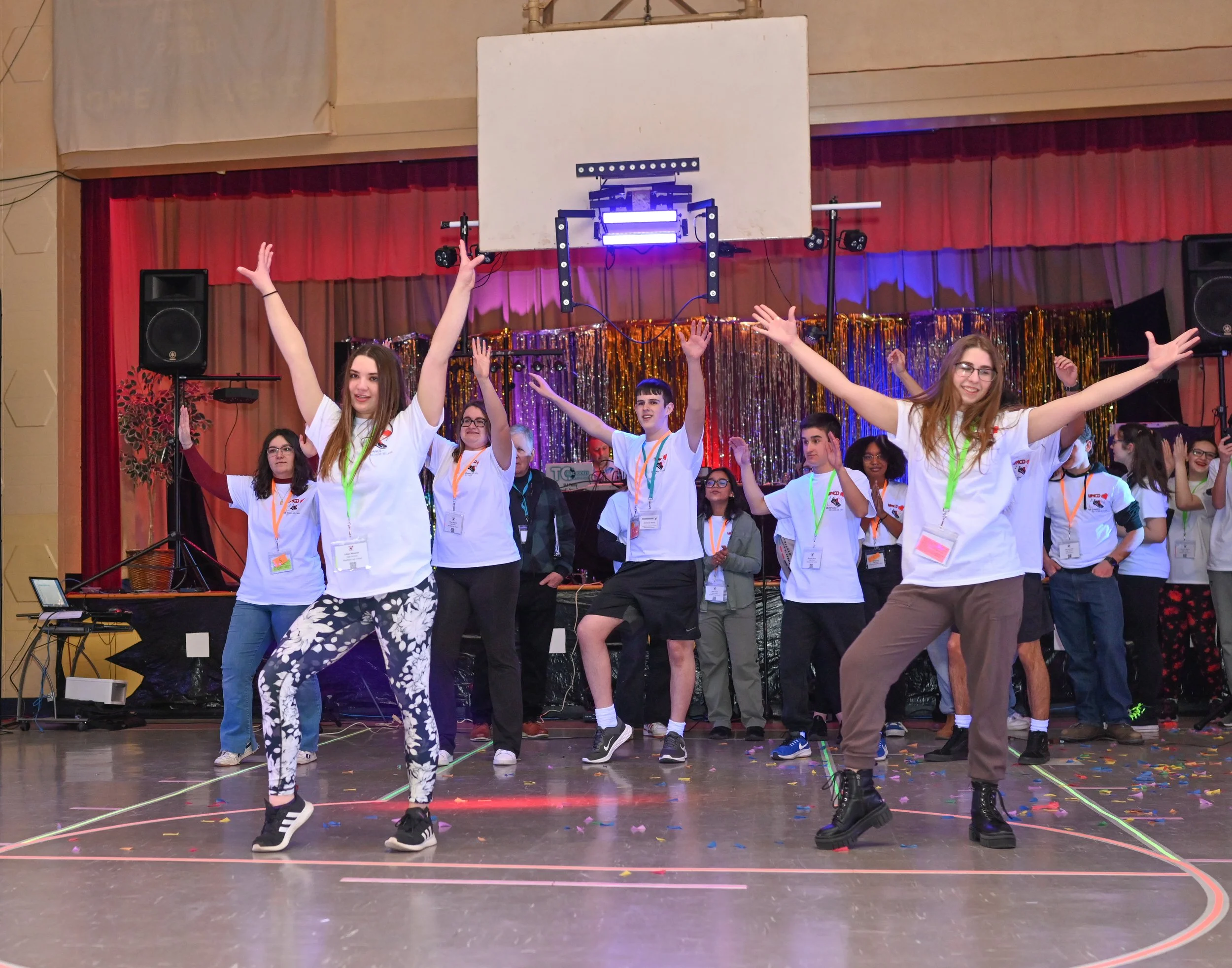 Group of young people dancing on a stage at an indoor event with party decorations and lighting.