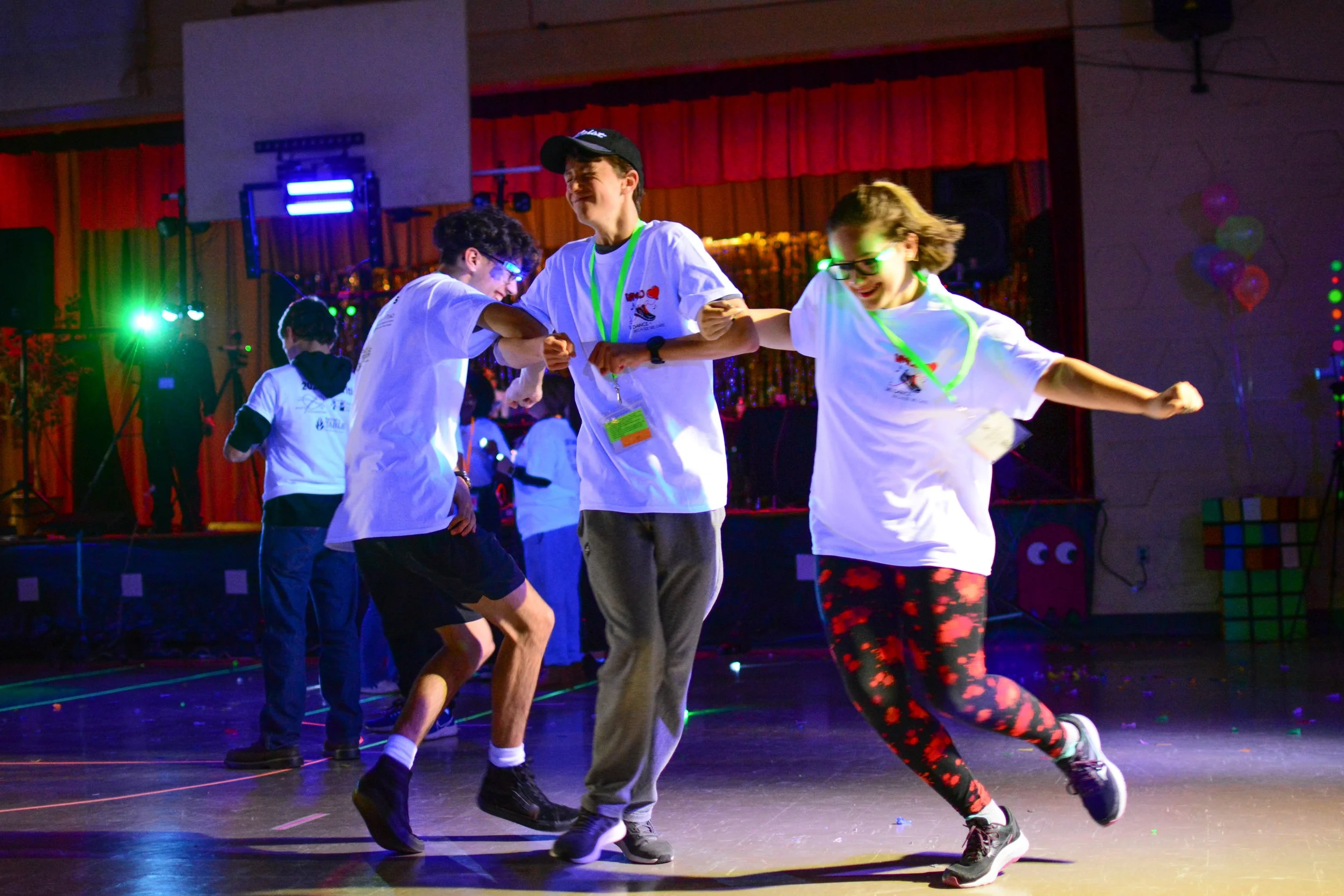 Children dancing and having fun at a party or event with colorful lighting and stage in the background.