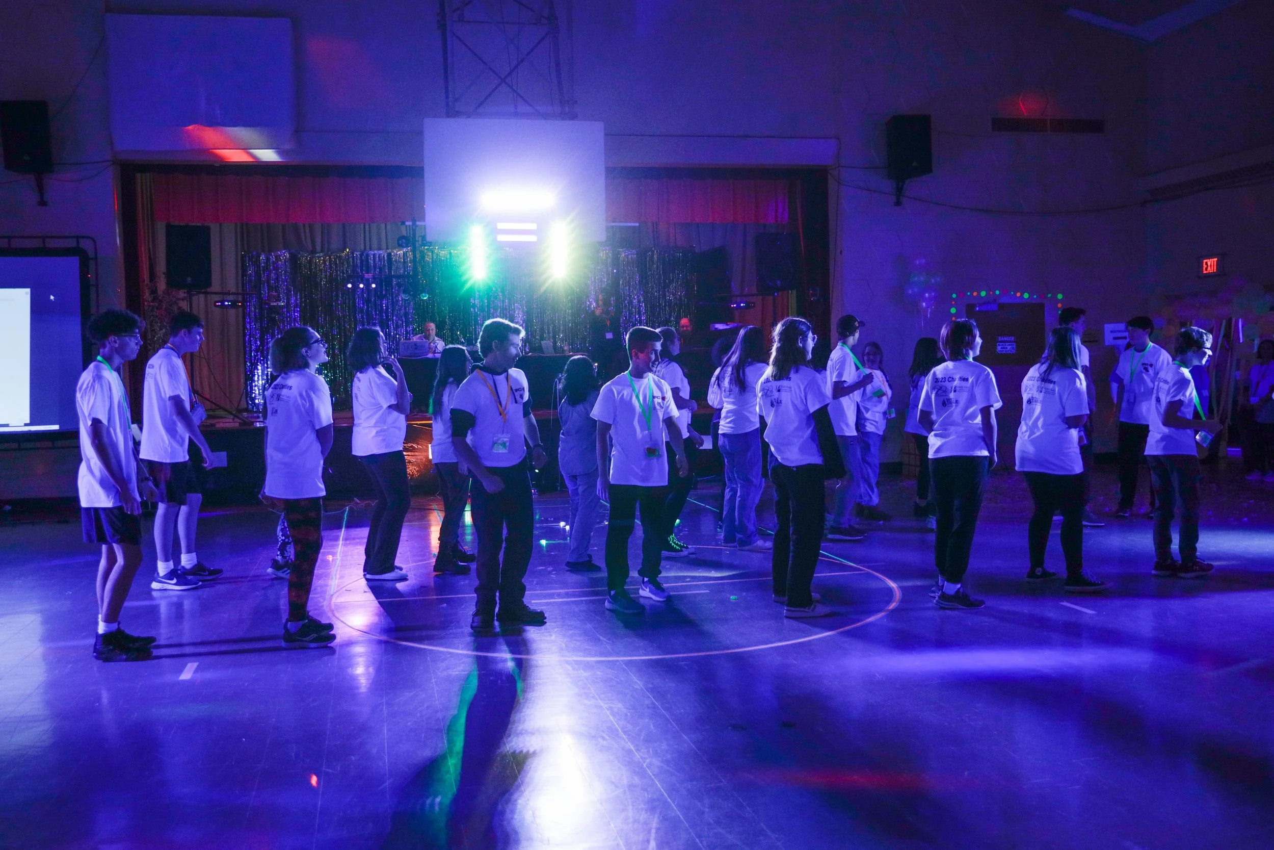 Students participating in a dance or exercise in a gymnasium with colorful lights and a stage in the background.