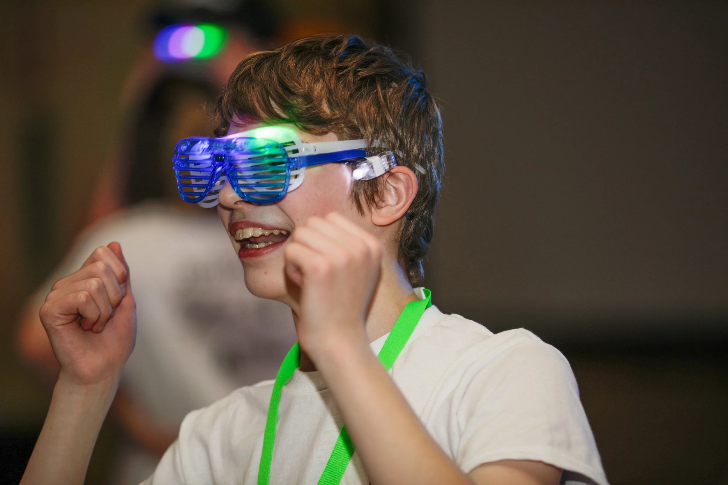 A young person wearing fun LED light-up glasses, smiling and celebrating at a party or event.