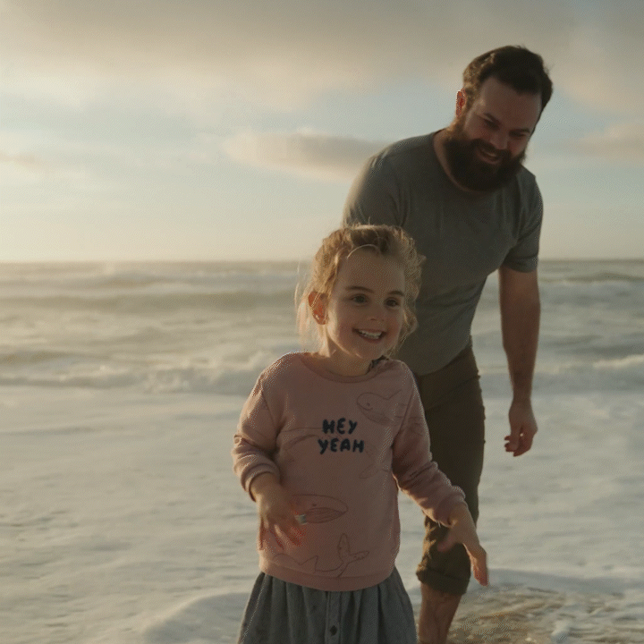 A man and a young girl enjoying time on the beach during sunset, playing near the waves.
