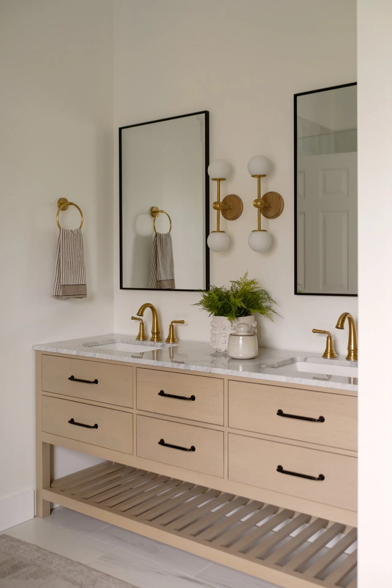 A bathroom vanity with a marble countertop, gold fixtures, two mirrors, and a decorative plant in a white pot.