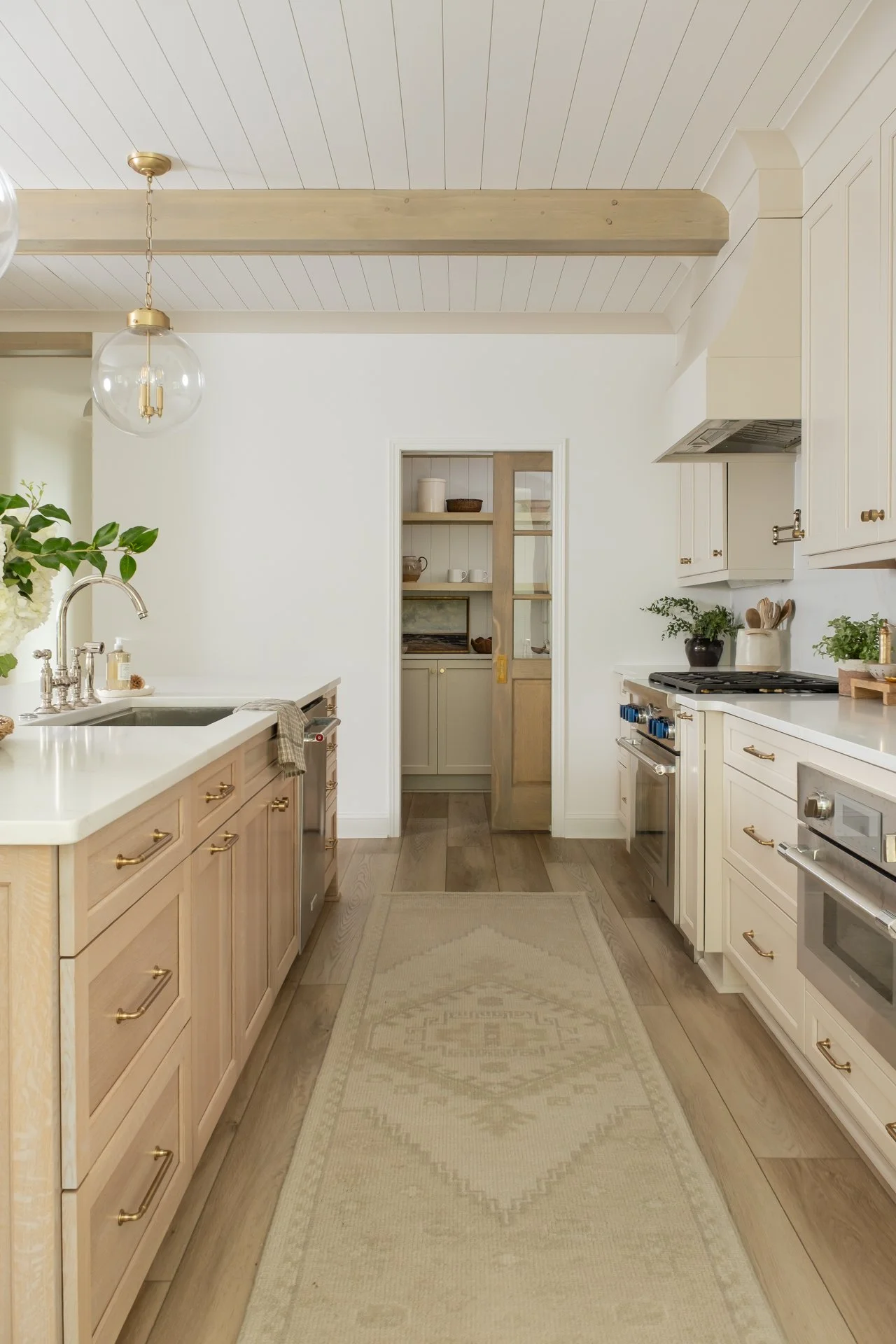 A bright kitchen with white cabinets, a light-colored rug, and a doorway leading to a pantry.