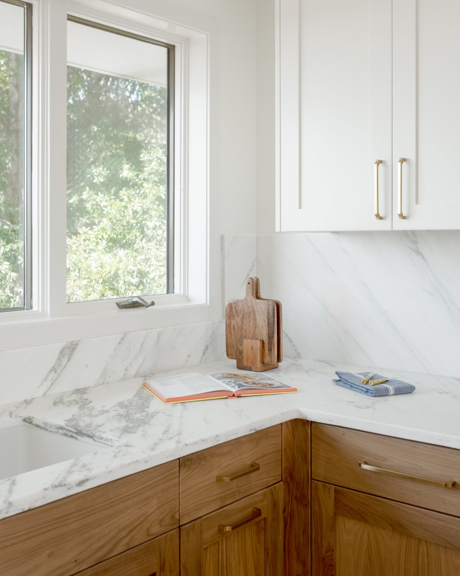 Kitchen with white marble countertop, wooden cabinets, window, cutting boards, book, and blue towel.