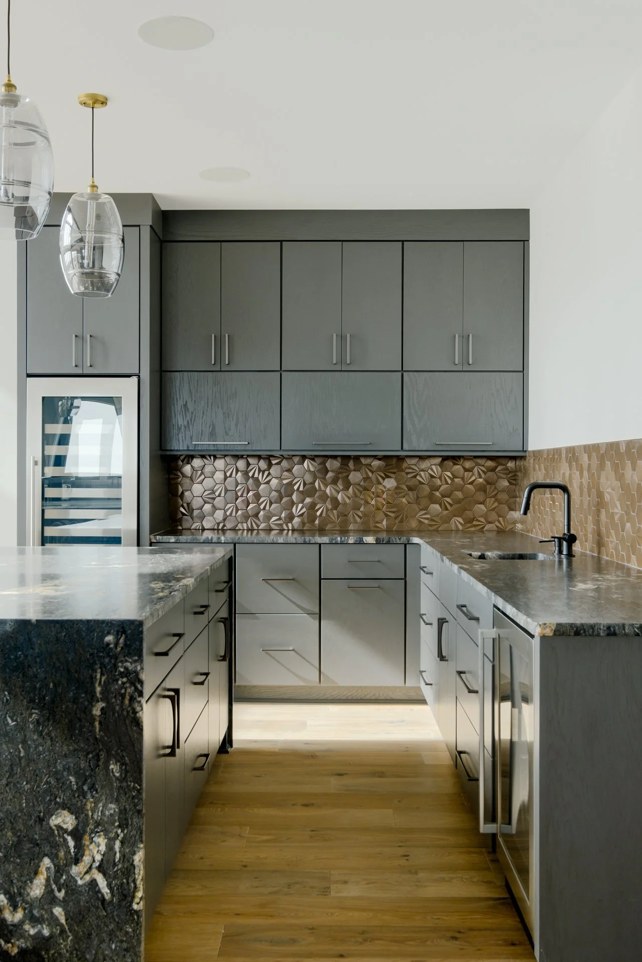 Modern kitchen with dark gray cabinets, copper backsplash, marble countertops, and wood flooring.