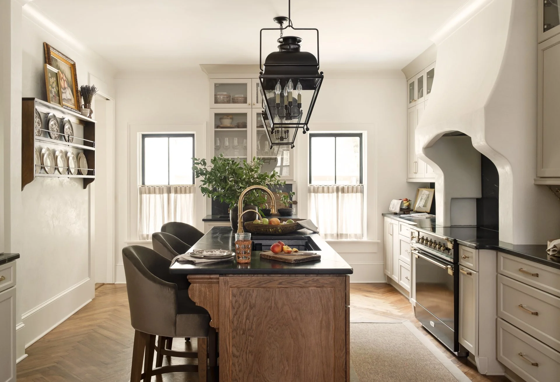 A kitchen with white cabinets, a black oven, a black kitchen island with a gold faucet, and natural light from two windows.