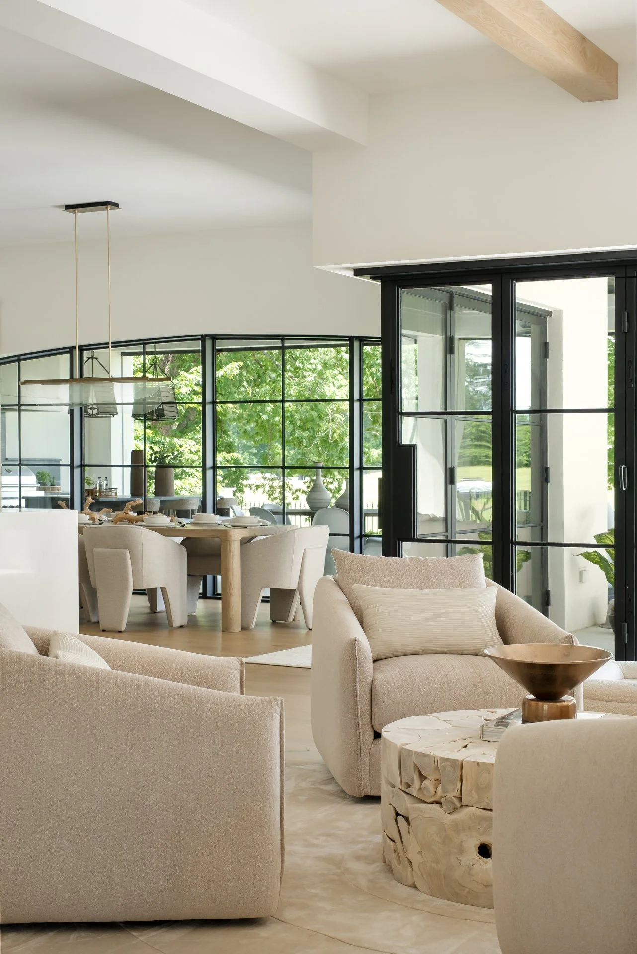 Bright living room with beige sofas and a carved wooden coffee table, with a large sliding glass door leading to a patio and a dining area visible in the background.