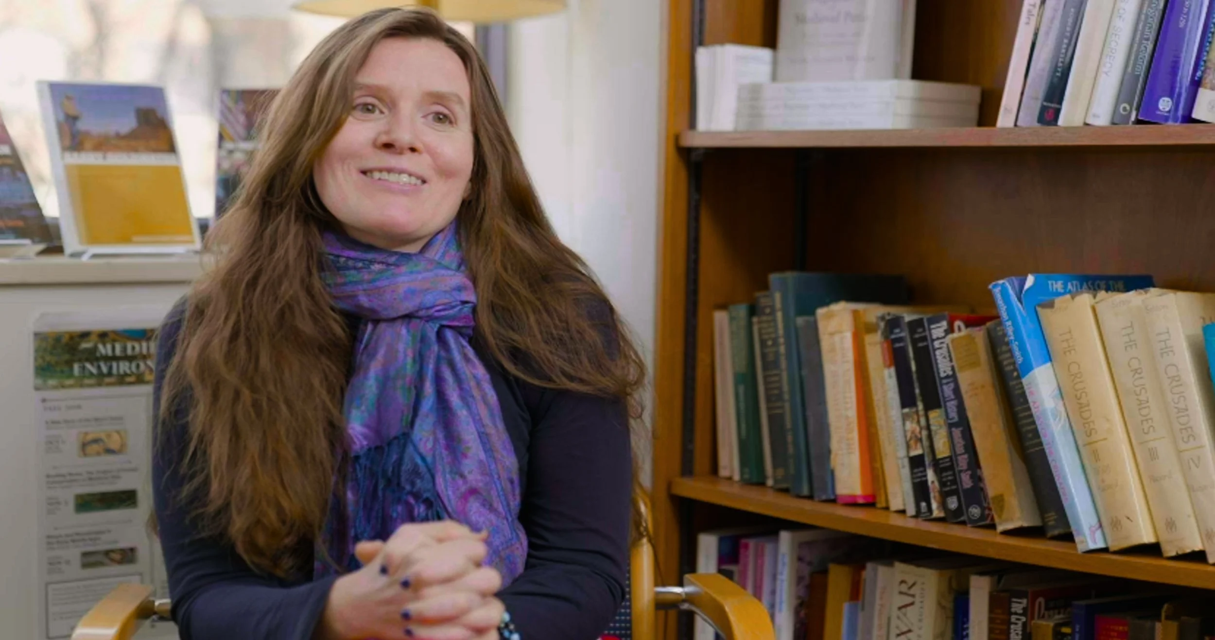 Interviewee smiling in front of a bookshelf. Still from The Real Cost, a student debt documentary directed by Sam Menendez and produced by Annie Menendez
