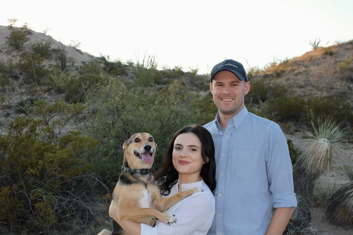 Chris and his wife Nora with their dog Wyck in the desert landscape of Resler Canyon with bushes and cacti.