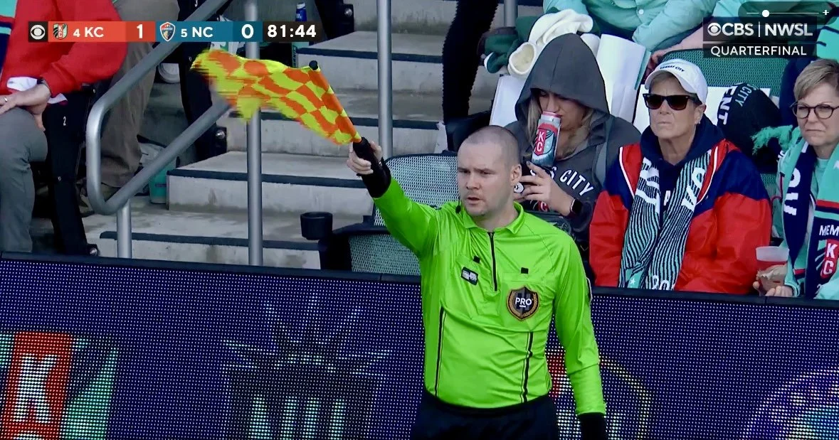 Chris working as a professional soccer referee, wearing a bright green uniform. The image is a screenshot of an NWSL game shown on CBS.