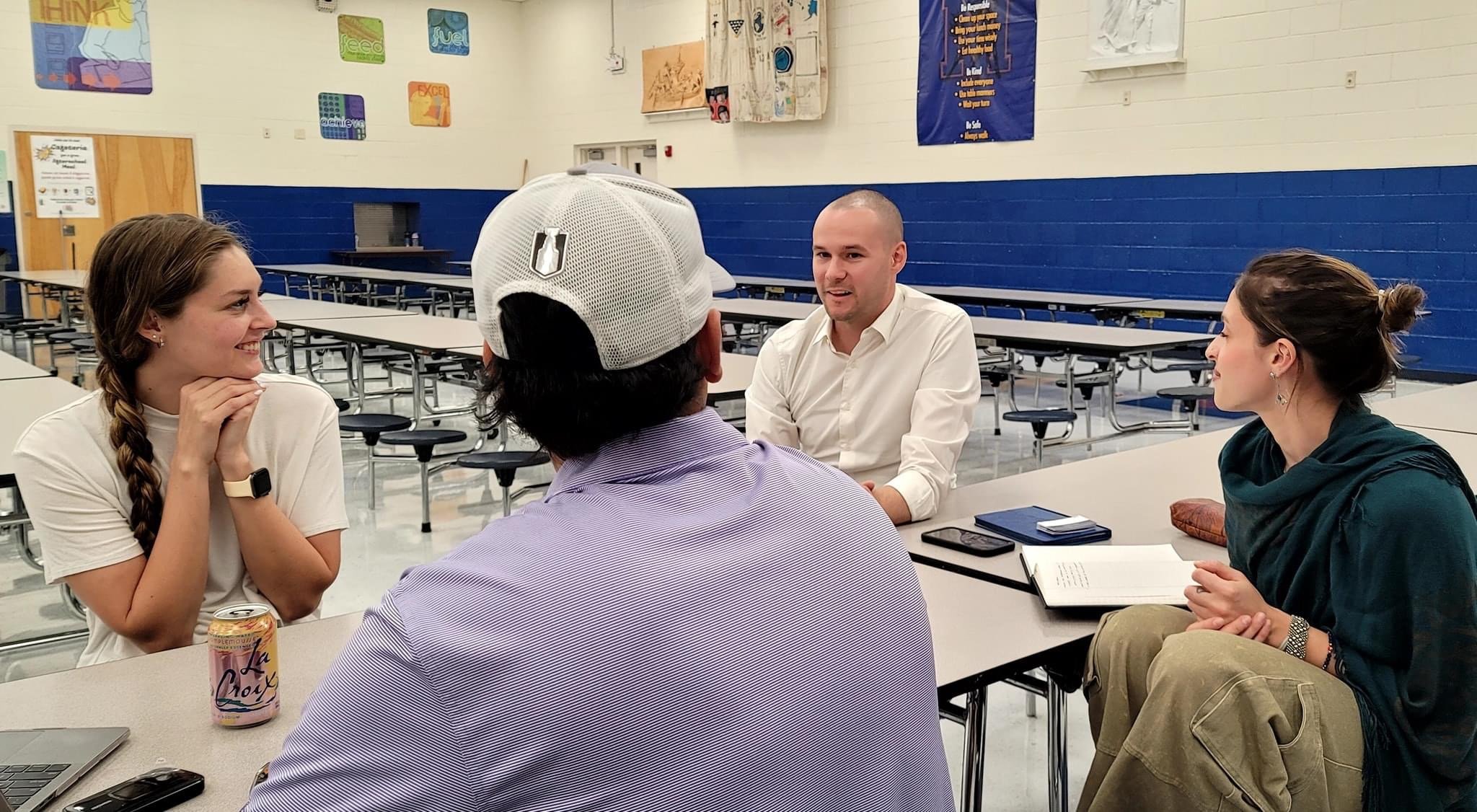 Chris speaking to a neighborhood association group sitting around a table at the Mesita Elementary cafeteria, engaging in conversation.