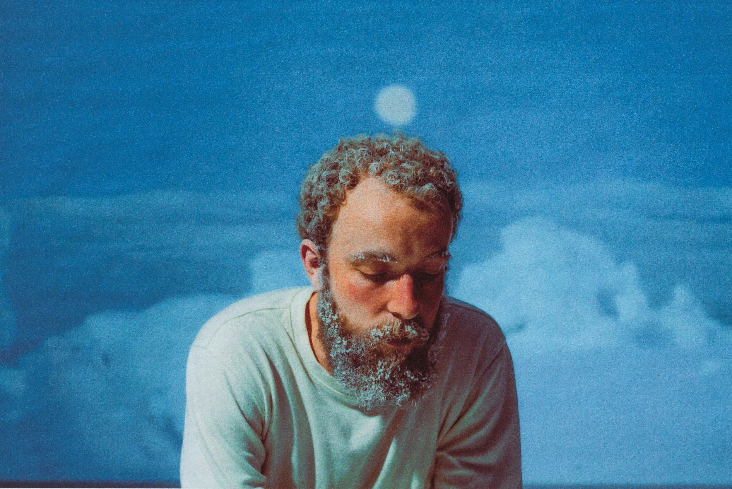 Young woman with dark hair styled in pigtails, light makeup with blue eyeshadow, and a green fuzzy top, standing in front of a backdrop with blue stars.