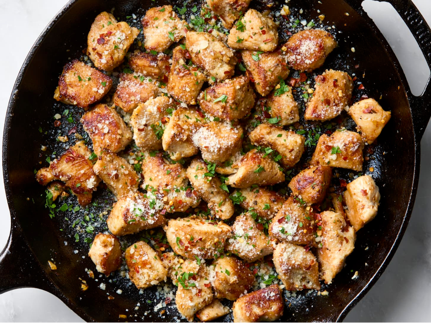 Cooked chicken pieces garnished with chopped herbs and grated cheese in a black skillet.