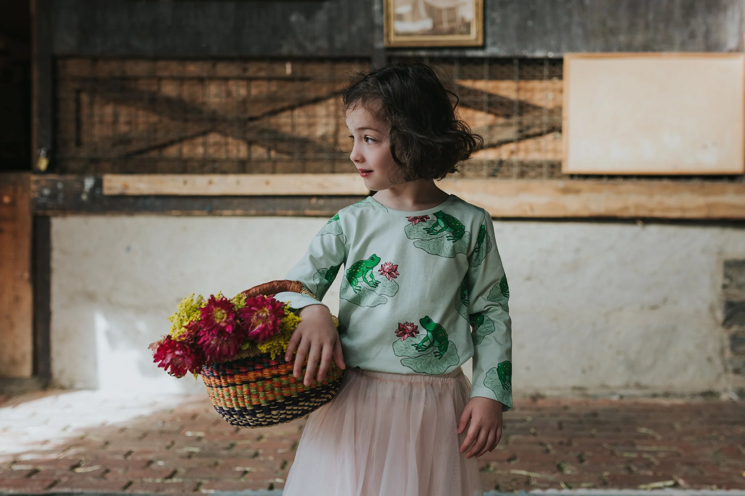 Young girl stands and holds basket of flowers.