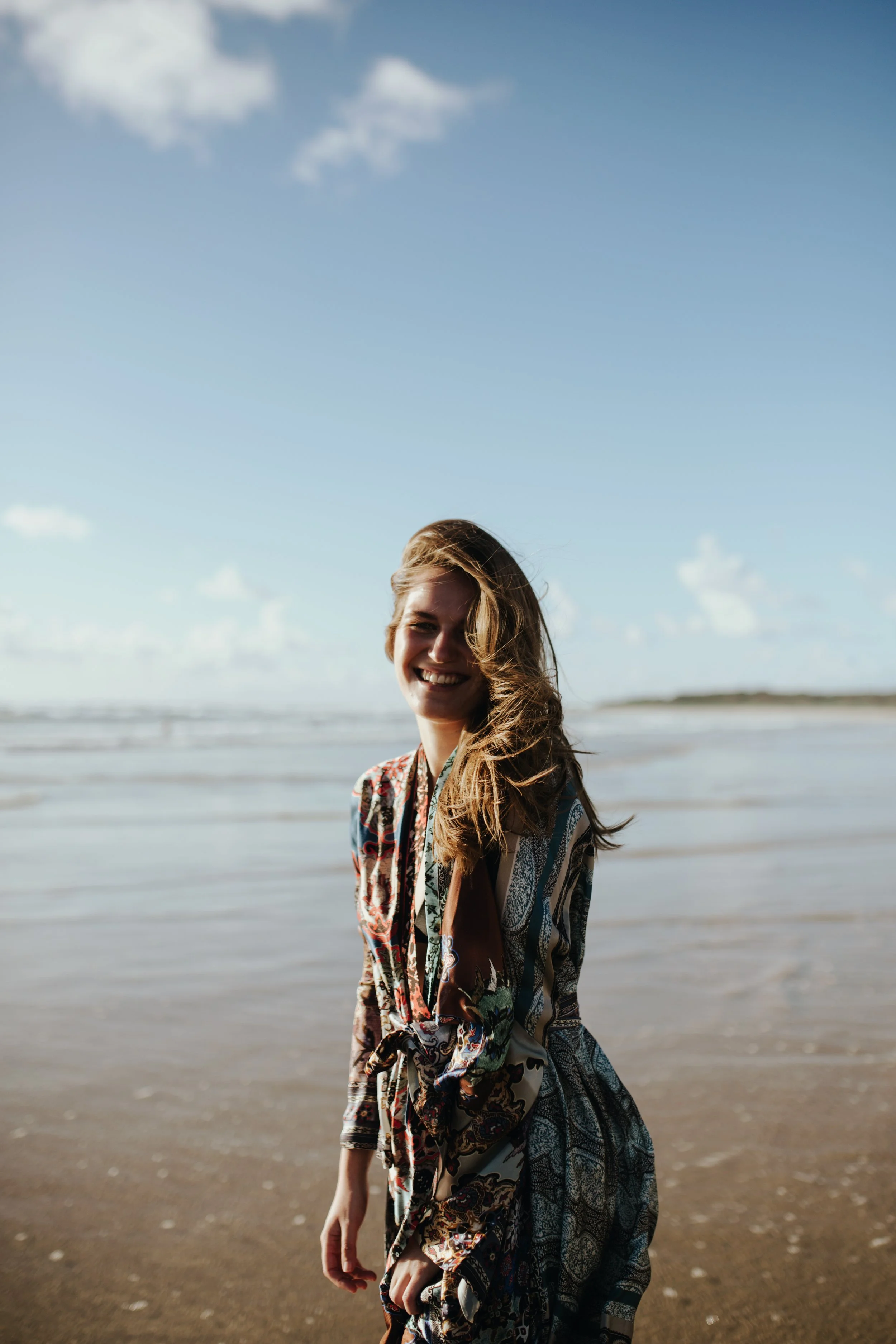 Model smiles into camera at beach on sunny day.