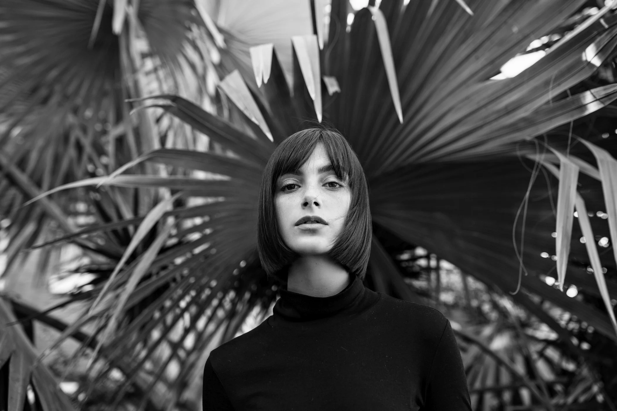 Model looks into camera in front of palm tree.
