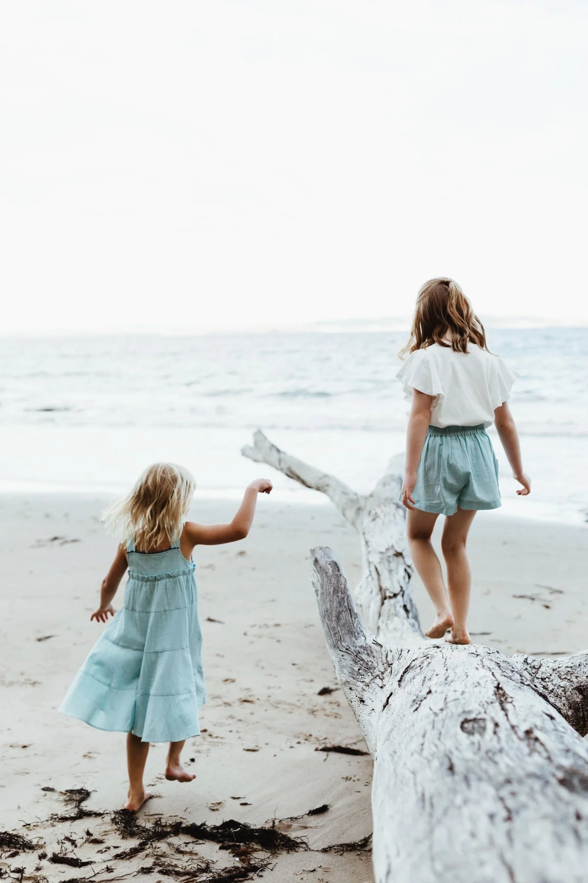 Girls play on driftwood at beach in Tasmania.