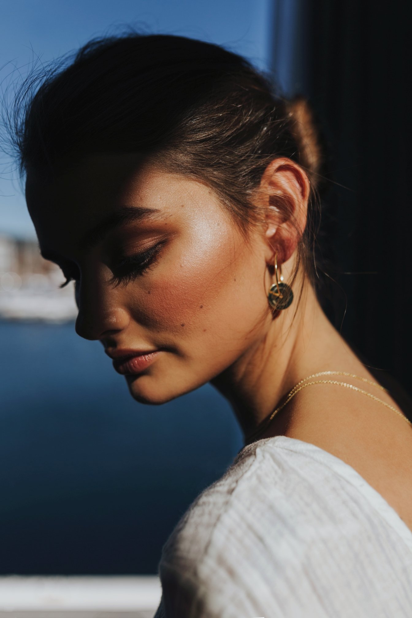 Model relaxes by window to showcase golden earrings during product photography.