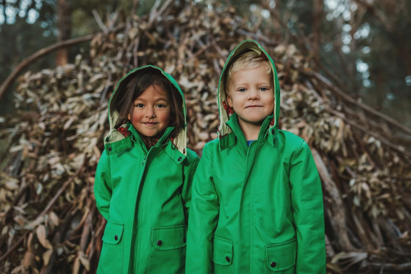 Two kids smile in green jackets in Melbourne.