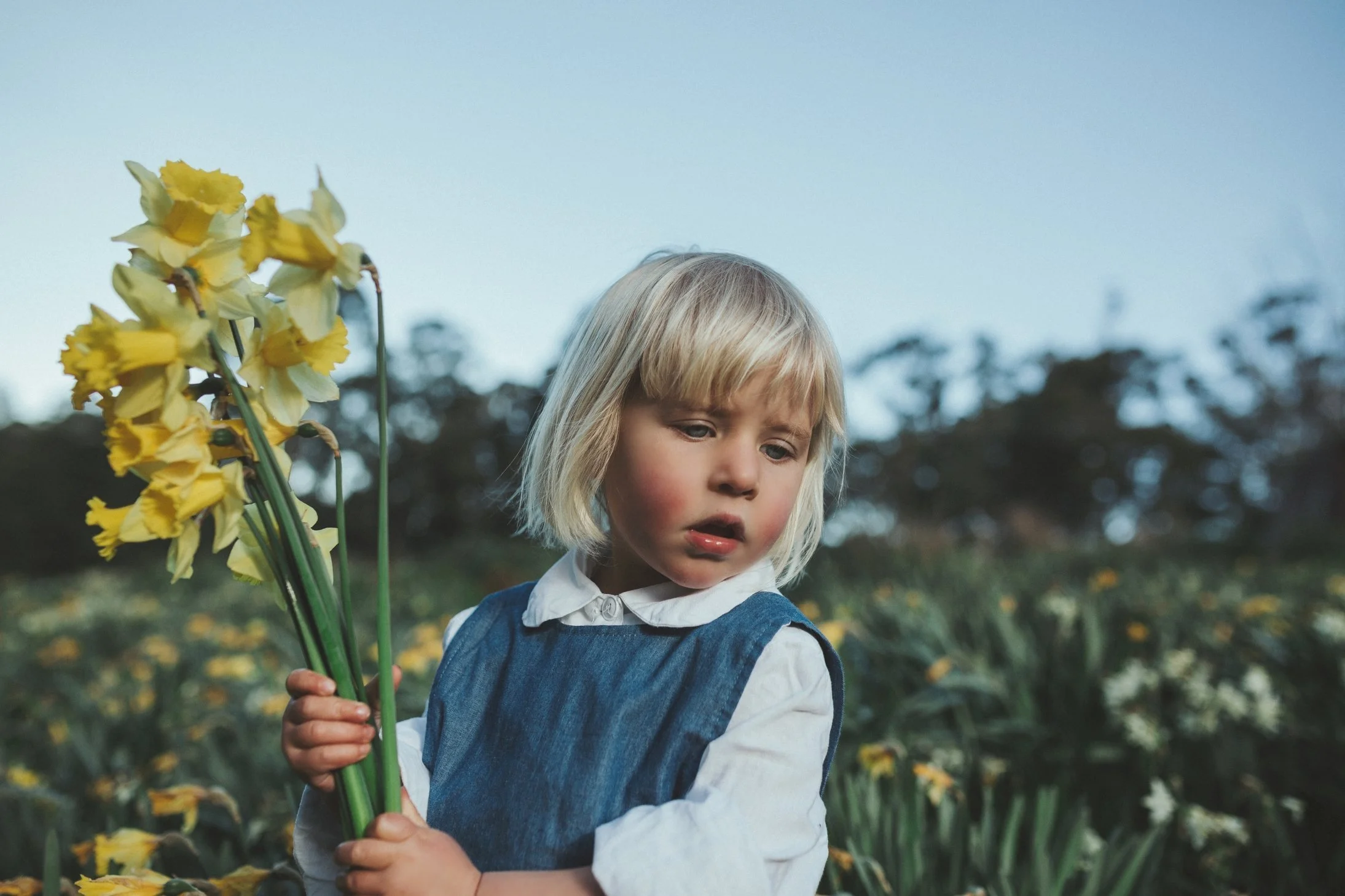 Girl carries yellow flowers wearing denim overalls.