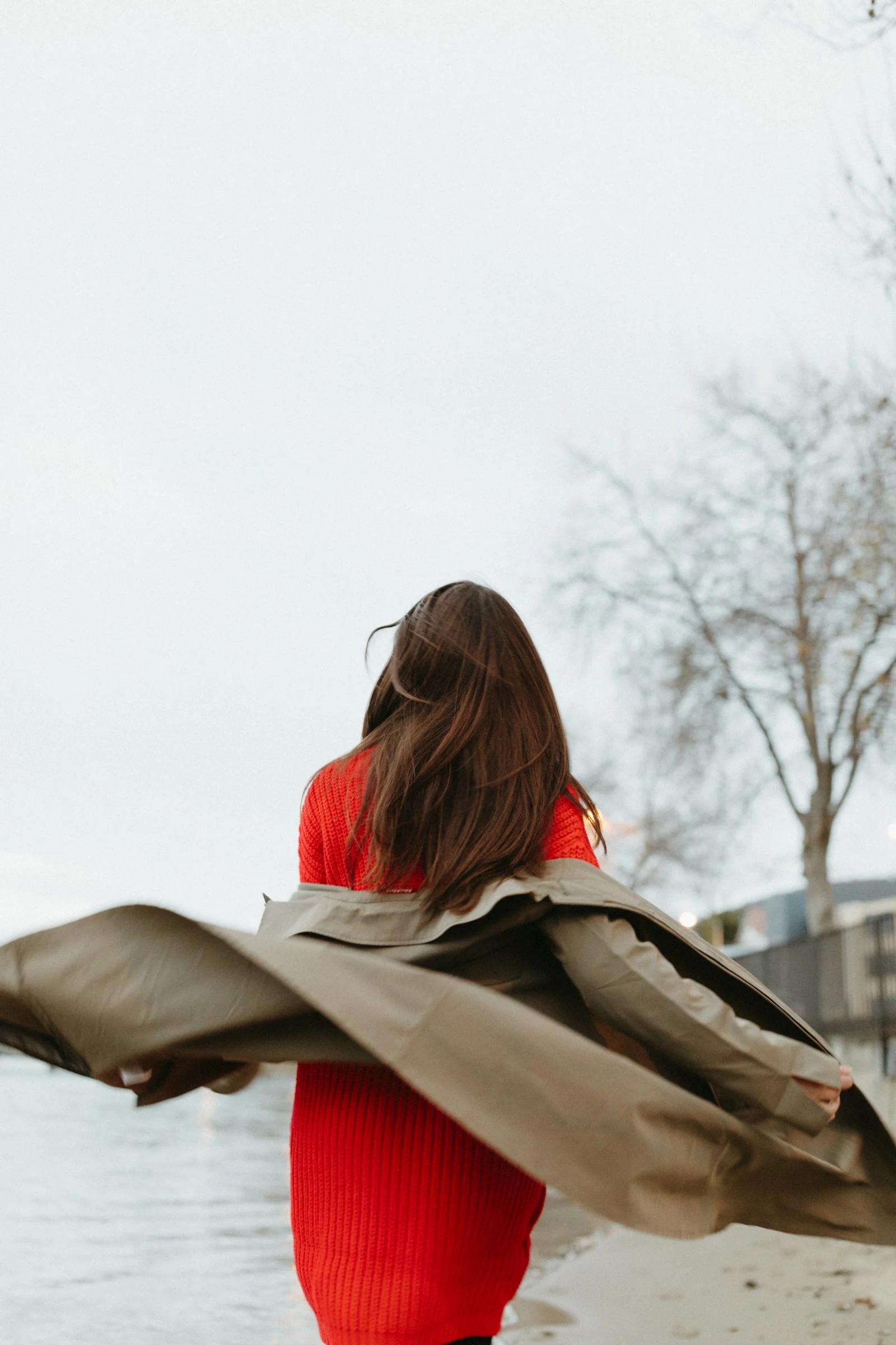 Woman runs by ocean edge in red sweater.