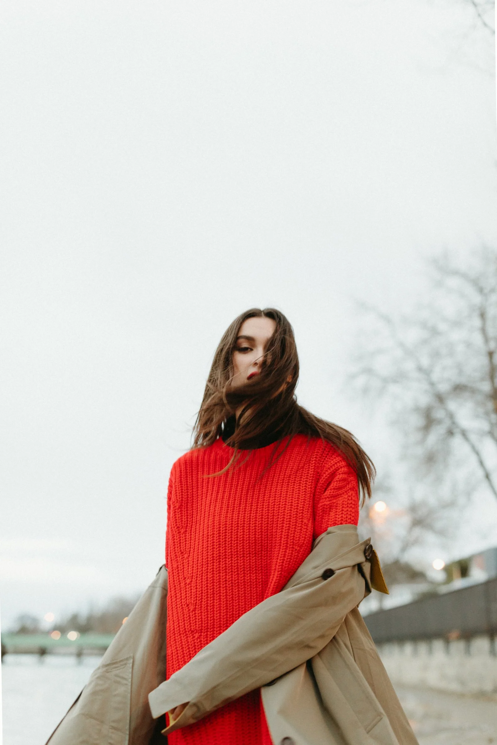 Model poses in trench and wind blows her hair across her face.