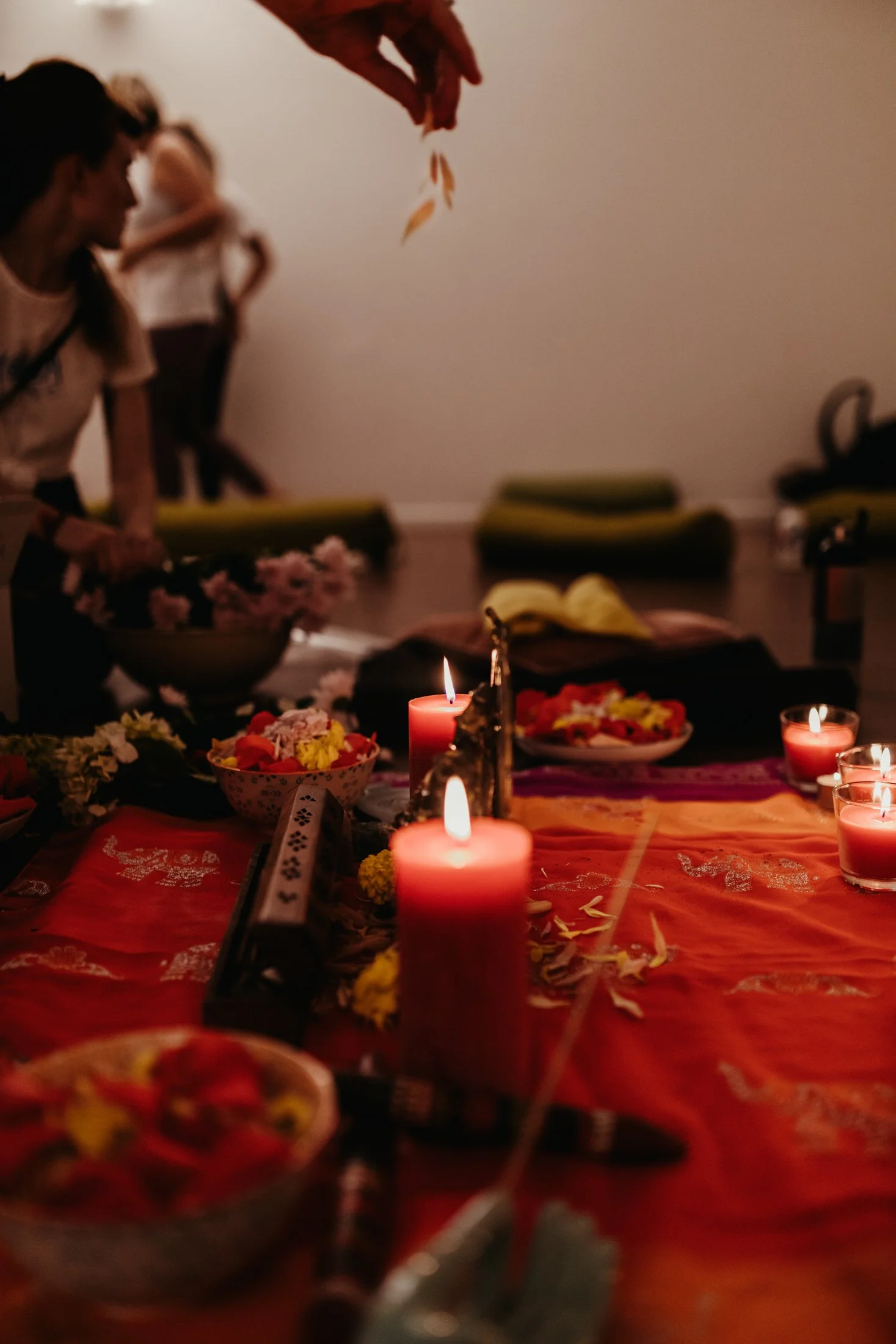 Hands drop flower petals onto mat with candles.
