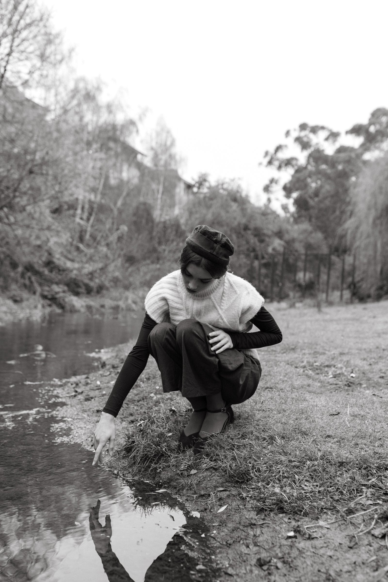 Woman reaches into rivulet with vintage outfit during fashion photo shoot.
