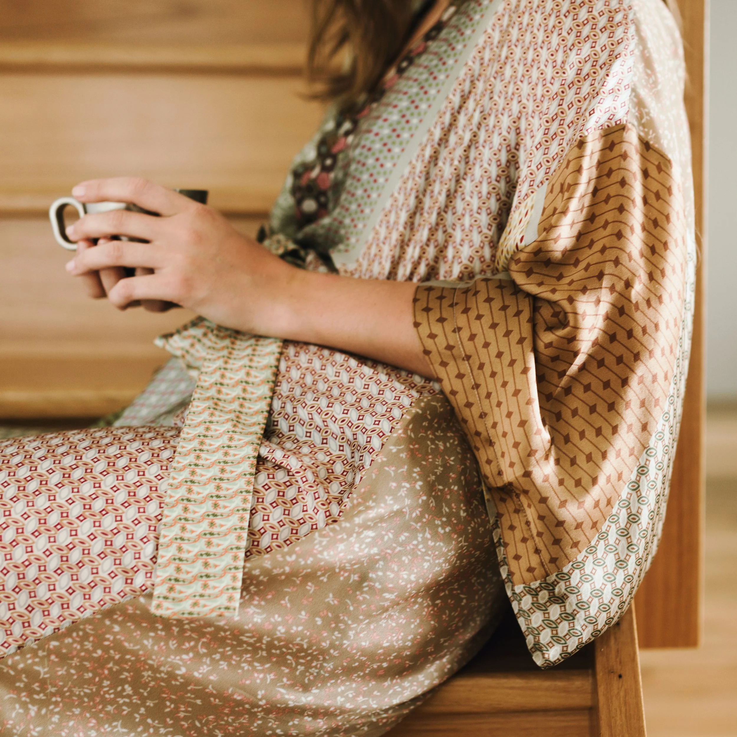 Model holds cup of coffee as she sits on stairs.
