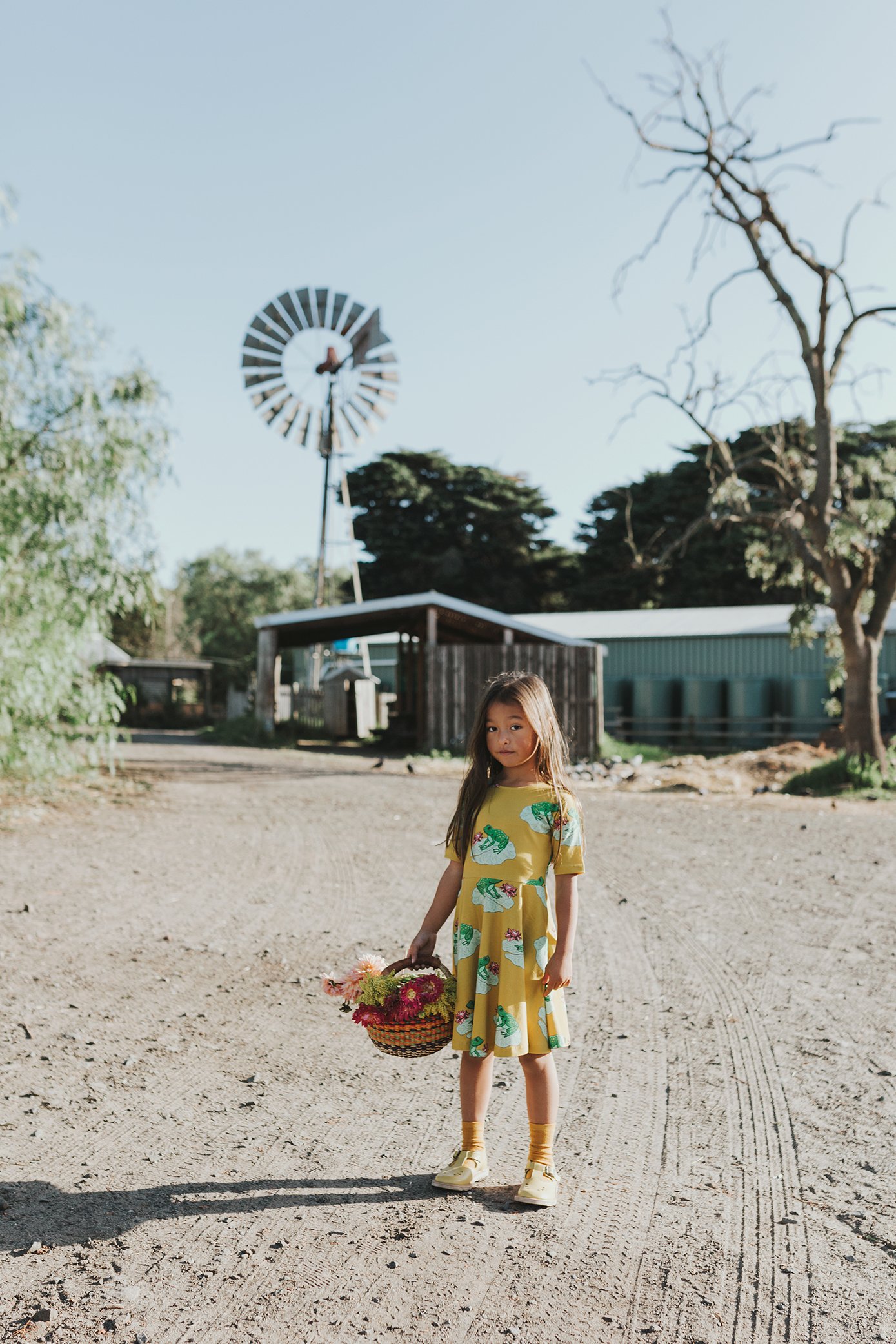 Young girl stands in front of windmill wearing colourful dress in Victoria.
