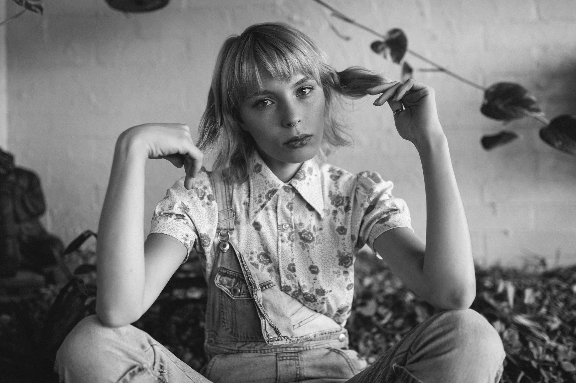 Model with bob hair cut sits in denim overalls.
