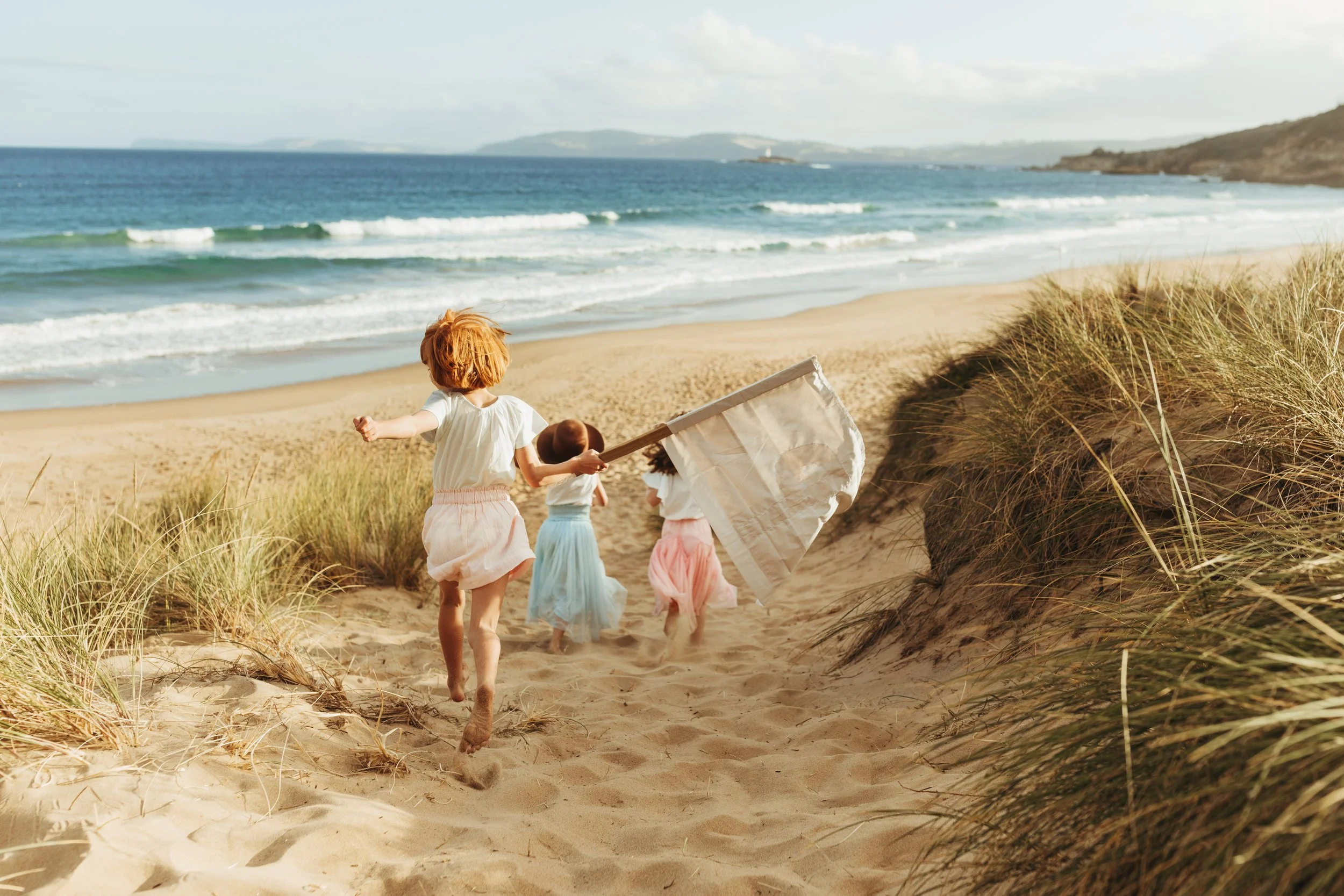Girls run down sand dune wearing pastel coloured clothes in Tasmania.