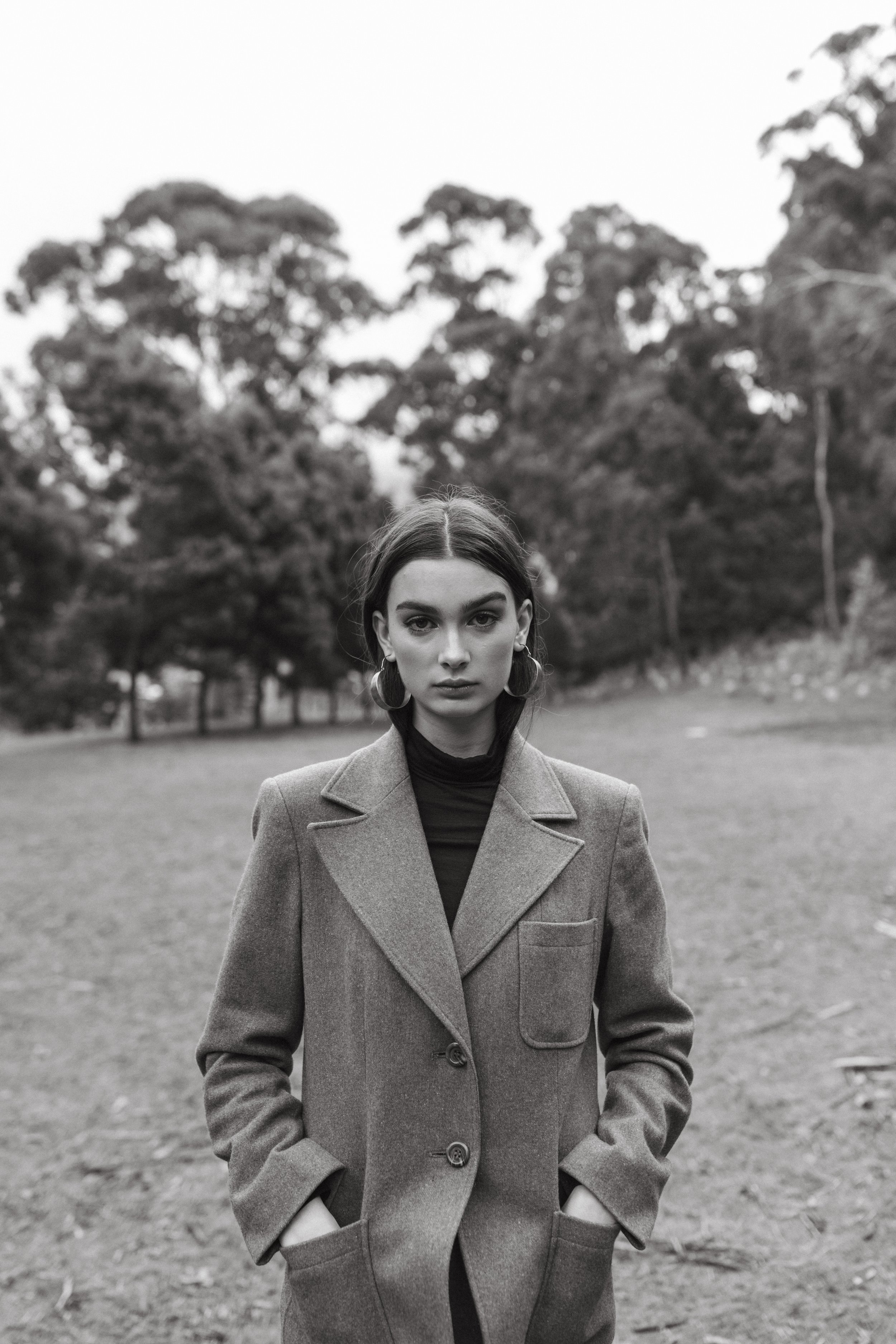 Model stands in open field with hands in pockets.