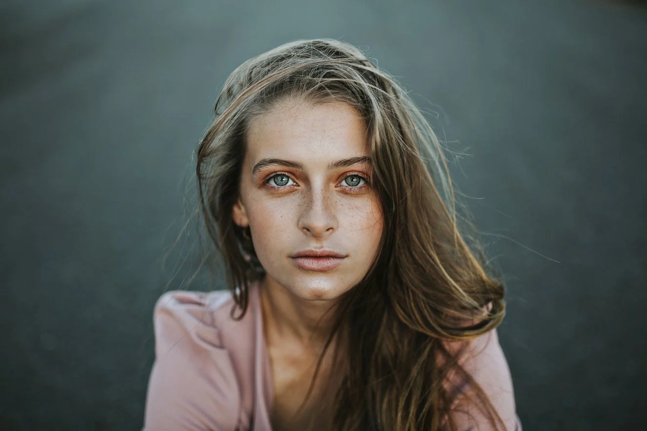 Woman sits on road in pink blazer looking up for model test photo shoot.