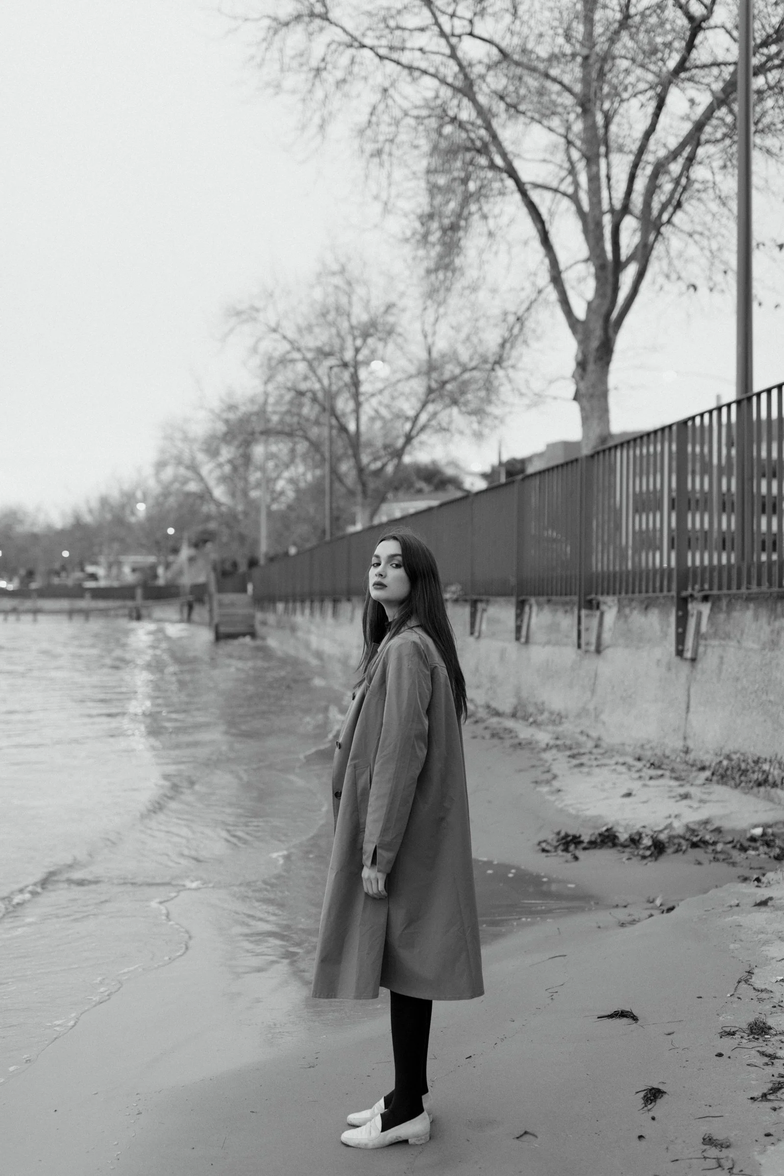 Model with long, dark hair in trench and white shoes.
