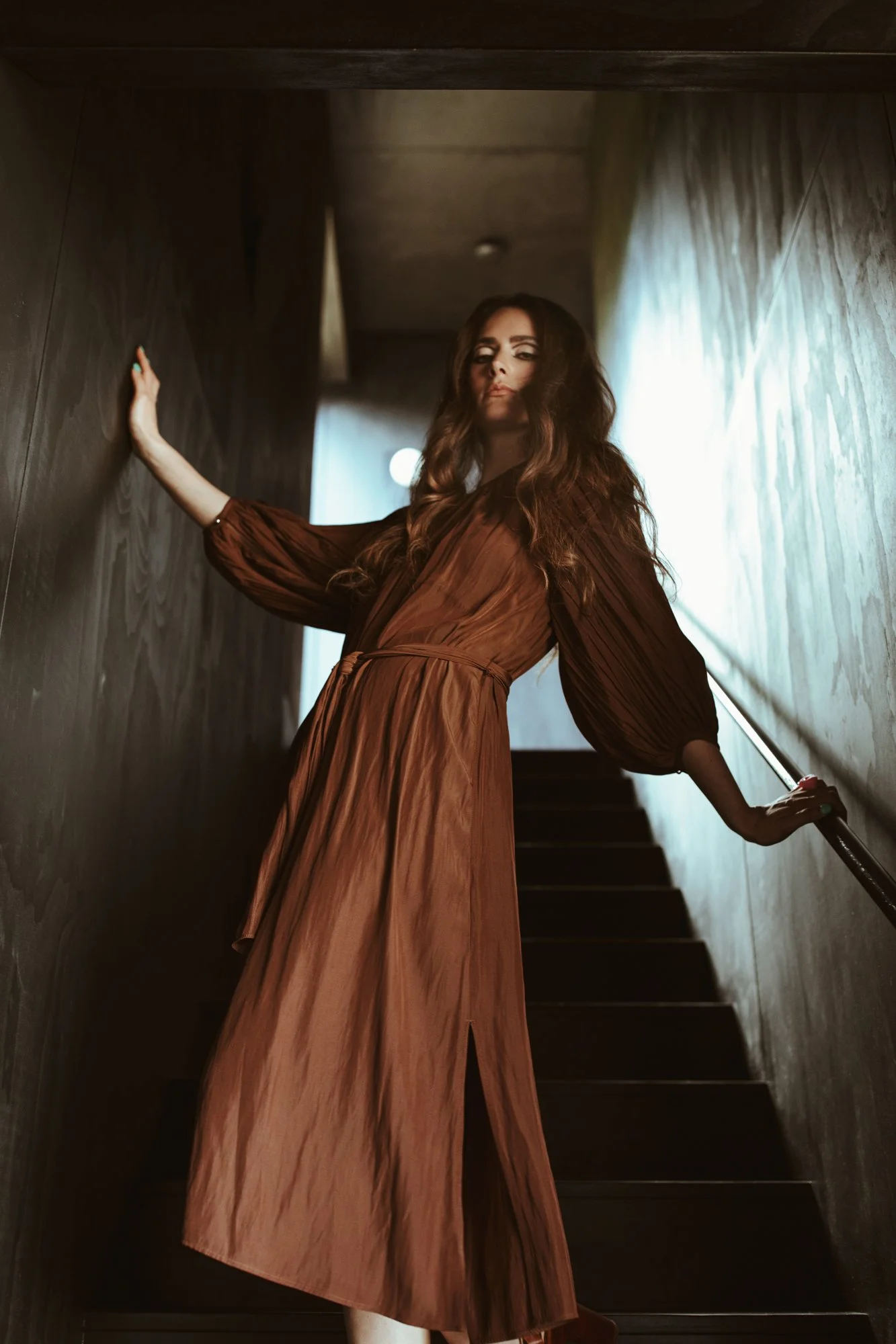 Model poses in stair case in brown silk dress.