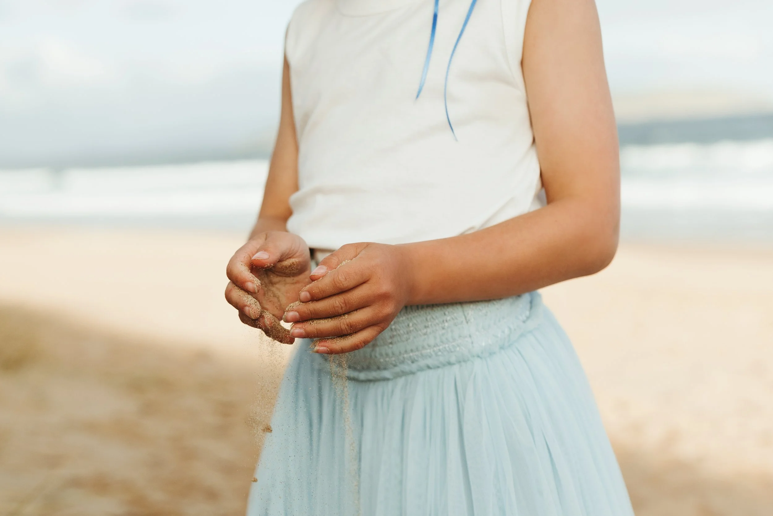 Child's hands letting sand fall through them at the beach.