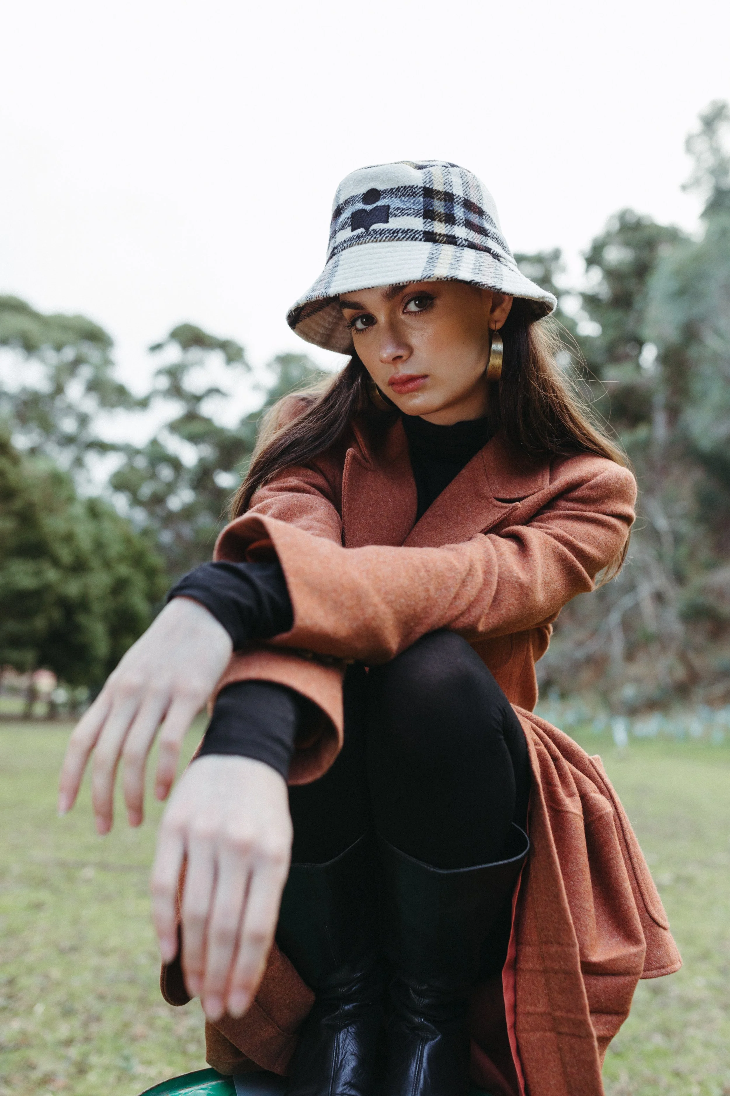 Model crouches with arms crossed in front of her and a bucket hat on.